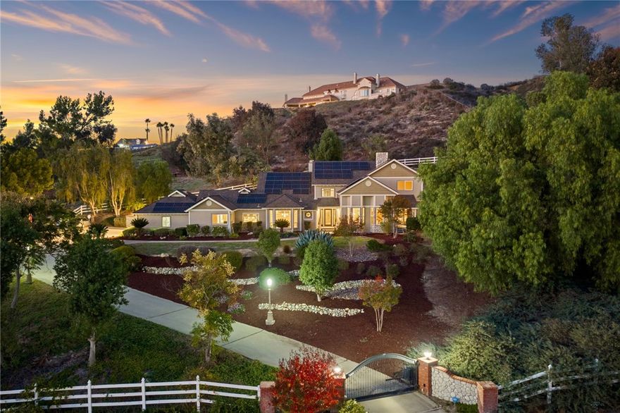 LOS RANCHITOS CUSTOM ESTATE!! ENJOY SWEEPING TEMECULA MOUNTAIN VIEWS AND BREATHTAKING SUNSETS from this five-bedroom Cape Cod–inspired home offering SOLAR and sitting on approximately 2.32 acres overlooking coveted South Temecula. A gated private drive leads to an elegant entry with a leaded-glass door, travertine flooring, soaring ceilings, plantation shutters, and thoughtful designer details throughout. The main-level primary suite enjoys its own private deck, a spacious walk-in closet, a jetted soaking tub, dual sinks with a vanity area, and generous linen storage. Two additional bedrooms offer en-suite bathrooms, while two more share a full bathroom with dual sinks and a walk-in shower. The home features a dedicated downstairs office and an expansive formal living room with a brick-accented fireplace, vaulted ceiling, and inviting window seats perfectly positioned to take in the breathtaking views or an afternoon read. The adjacent formal dining room enjoys spectacular views from oversized windows and is enhanced by a chandelier set within a ceiling medallion and framed by crown molding. The beautifully designed kitchen showcases granite counters, a hooded cooktop with tile backsplash, a pot filler, a trash compactor, stainless steel appliances, a GE Monogram built-in refrigerator, a bay window, a large built-in buffet with storage, and a charming breakfast nook. Overlooking the dining room is the warm and welcoming family room, complete with a second fireplace and two sets of double doors opening to a covered patio with a gas firepit, creating a seamless indoor-outdoor living experience! Just off the kitchen, the lower backyard hosts a built-in BBQ island with bar seating—ideal for effortless summer gatherings—while the expansive rear and side yards offer abundant space for a pool, sport court, barn, RV parking, or other custom amenities. With nearly 3,800 square feet of living space, this home offers comfort, versatility, and room for multi-generational living. Located in the prestigious Los Ranchitos community—known for its horse trails, custom estates, and unbeatable proximity to Temecula’s dining, shopping, award-winning schools, wineries, and entertainment—this exceptional slice of Southern California is one you won’t want to miss. Schedule your private tour today.