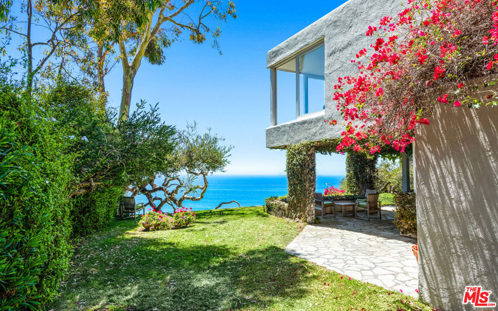 Extremely rare blufftop contemporary on the market for the first time in 50 years. Very private and set above beautiful Dume Cove at the end of a long drive, this nearly one-acre garden property commands sweeping views of ocean, islands, and coastline. Mature trees, vast wraparound lawns, and manicured gardens offer an idyllic oceanfront setting for outdoor entertaining and recreation. The home's comfortable, open-concept interior features a triangular, double-height entry, high ceilings, gallery walls, large windows, and hardwood floors. In the ocean-view living/dining room, there is a wall of library bookshelves to the ceiling, a woodburning fireplace with a recessed wood-storage area below the tiled hearth, plus a built-in bench and corner reading area with full-height windows on two sides. In the dining area, additional windows and doors open to the backyard and a covered flagstone patio for al fresco dining and entertaining. Nearby, the kitchen has butcher-block countertops with corner windows facing onto the covered patio and ocean, plus a Wolf range and tiled wall and floor. The home's strong architectural lines carry upward to the second floor, with an angled wall of windows, another floor-to-ceiling bookcase, and the tranquil bedroom suite, with huge, sliding ocean-view windows on three sides. In addition to a two-car garage, the front of the property has a huge lawn with ample space for large gatherings. This wraps around to a flagstone patio at the side of the house and into the stunning, ocean-facing backyard, where a path leads to a bench for whale watching and star gazing, plus steps that lead down to the pristine white sands of Dume Cove. Quiet and private, this is truly a Point Dume gem.