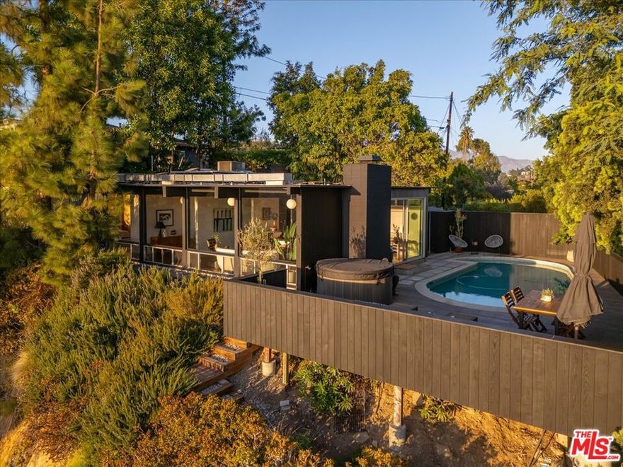 Tucked away on a secluded road, this hillside Neutra inspired Mid-century modern home offers exceptional privacy, striking design, and sweeping panoramic views. Thoughtfully preserved and tastefully updated, this home features clean architectural lines, exposed beams, and expansive floor-to-ceiling windows that fill the interiors with natural light. The open living area centers around a classic mid-century fireplace, creating a warm and inviting focal point. Spacious yet intimate, the layout flows effortlessly from the living and dining spaces to the outdoor deck, ideal for relaxing or entertaining against a backdrop of soaring views. Outside, a private pool is framed by custom decking providing generous space for lounging and tranquil evenings under the stars. Set among pine trees visited by red-tailed hawks, the property offers a rare and unique connection to nature. With its blend of iconic design, modern comforts, and a rare sense of seclusion, this home is a peaceful retreat just minutes from everything... yet feels a world away.
