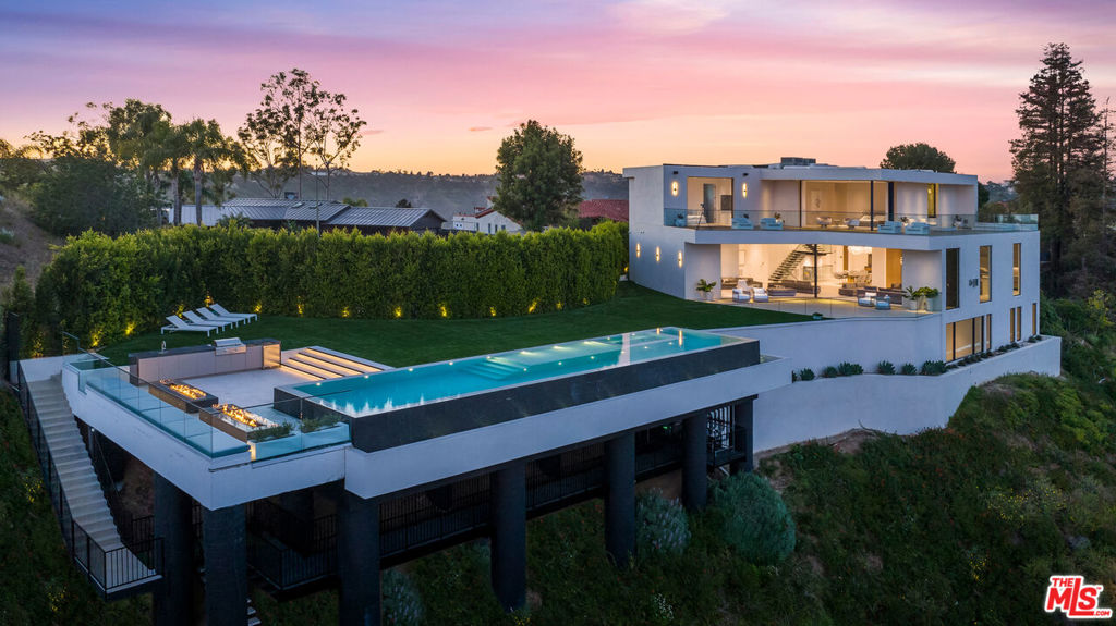 Recently completed and masterfully executed with the finest materials, this 5 bed, 10 bath luxury contemporary on an irreplaceable flat promontory lot adjacent to Beverly Park features head on city and 360 degree views. Spanning more than 8,500 sq. feet, automated walls of glass provide endless views and seamless indoor-outdoor flow to an expansive yard, 60ft infinity pool, and ultimate sunken entertainment area with 2 firepits. Remarkably scaled, the double entry and elegant glass staircase leads into the main living areas with book matched marble fireplace, lounge, bar, dining, and office. A chef-grade kitchen features dual 12-foot quartzite islands, Gaggenau appliances, double refrigeration wall, with seamless cabinetry. The primary suite is appointed with dual spa-grade bathrooms, closets and private terrace. Four additional luxurious oversized ensuite bedrooms with beautiful views, are situated throughout the residence affording dedicated privacy. For ultimate living, a sleek glass walk-in wine cellar, a plush theater with stadium seating, a dedicated fitness studio, elevator, and smart technology systems complete the residence. The unparalleled site and quality of this modern estate cannot be duplicated.