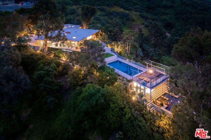 Available fully furnished and turnkey for short, midterm, or long term lease! Rustic and urbane, old-world and high tech, where rural estate meets downtown elegance in this once in a lifetime sensory immersion experience. Escape from ordinary down the a private driveway to the gravel motor court, earthy stone fascia, and arboreally adorned grand entrance to the exquisite execution of this contemporary hillside estate. Natural light will greet you in virtually every corner of the dramatically-styled indoor-outdoor open plan living spaces with floor to ceiling glass walls that reveal resort-style landscaping and marvelous canyon views. You will cherish every moment in the spacious living room with its uplifting fireplace, family room, dining room, gourmet kitchen with professional appliances, custom cabinetry and breakfast, and covered patio. Indulge your inner sun-worshiper on the rear lawn and wood deck or beside the shimmering pool in the viewing pavilion. Retreat to the opulent primary suite, nestled in pastoral splendor and featuring a fireplace, large walk-in closet and dressing area, and picturesque bath with dual basins, spa tub, and steam shower. A guest/maid suite with bath and laundry room is located off the kitchen and two additional guest rooms with a shared bathroom are available for your family and friends. A detached guest house with bedroom, bath, kitchenette and private patio with koi pond is available for extra special guests or private getaways. Expertly decorated with curated artwork and careful attention to the balance between color and texture and light and dark, as you ensconce yourself in a perpetual source of positive energy day and night, whether you're entertaining, working, or relaxing, alone or with family and friends. Located on a cul-de-sac off of Stone Canyon and tucked away in the gorgeous hills of Bel Air, this one-of-a-kind domicile is an encounter to remember.