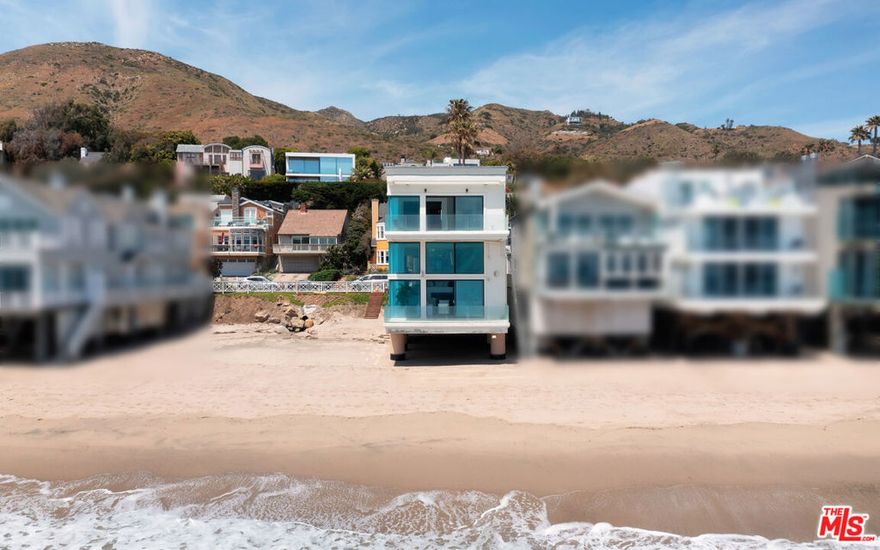 A sleek contemporary with walls of glass and majestic ocean, shoreline, and island views, this sensational home is designed for heavenly relaxation and sophisticated entertaining. Built on three levels for maximum enjoyment of the sunrise-to-sunset panorama, the home's wraparound windows, exceptionally high ceilings, and gorgeous furnishings provide a tranquil setting on the sandy shore of Sea Level beach. The entry, with a huge pivoting glass door, opens onto a mezzanine with a small seating area. Steps lead down to the lower level, where the enormous living room has floor-to-ceiling windows on two sides, a tiled bar, handsome built-ins, and wide glass doors that slide open onto a lighted beachfront balcony with ample room for dining, entertaining, and sea- and star-gazing. Also on this level is a powder room, laundry, and a bedroom. From the foyer, steps lead up to the middle floor, which is home to a beautiful chandelier dining area, chef's kitchen, and the primary suite. The kitchen is equipped with top-quality appliances, an island with bar seating, sleek built-ins, and a walk-in pantry with a beverage cooler. The primary suite is a spacious and private retreat that commands spectacular views and opens onto a large oceanfront deck. The suite has a built-in beverage cooler, walk-in closet, and a lovely spa-style bath. A skylight stairway leads to the top floor, home to a television/reading lounge and three bedrooms, one with a private balcony. The home is also equipped with smart-home features, multizone air conditioning, built-in speakers, a two-car garage, and a stairway to the beach below. This is a stunning new oceanfront residence and the perfect setting for comfortable living and generous entertaining.