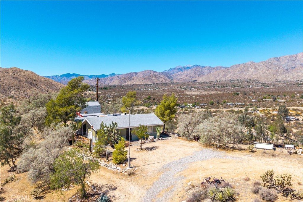 Gorgeous two-bedroom, one-bath home perched on a hilltop with 360° panoramic views! As you pull up to the property, you’ll immediately notice the incredible vistas that surround the home—rolling desert hills, open skies, and unmatched privacy. Step inside and prepare to be wowed by the vaulted tongue-and-groove ceilings and the stunning bank of windows that perfectly frame those breathtaking views. A cozy wood-burning stove sits in the living room, perfect for chilly winter evenings, while stylish hexagon tile flooring flows throughout the space and into the primary bedroom. The primary bedroom continues the theme of high ceilings and expansive windows, making the most of the natural light and open feel. The centrally located kitchen offers plenty of cabinet space, great storage, and a designated dining area. What makes this room truly special is its access to two separate patios, one north-facing and one south-facing, so you can enjoy sun or shade any time of day. The second bedroom is nicely sized and, like the rest of the home, offers that same incredible view. The bathroom has been tastefully remodeled with a beautiful tile walk-in shower, giving it a modern yet timeless feel. Step out onto the southern-facing patio and you’ll find a large wooden deck shaded by mature trees, creating a private and serene outdoor oasis. It’s a magical spot to relax, entertain, or simply soak in the scenery. To top it off, there’s a large detached barn for additional storage or potential creative use. All of this sits on a full five acres with its own well—plenty of space, privacy, and potential in a one-of-a-kind setting.