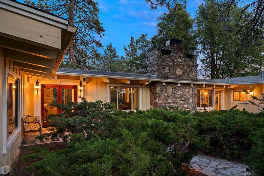Perched atop a mountain ridge is a single-story, mid-century executive retreat offering a wall of windows showcasing majestic mountain tops and iconic Lily Rock. From the circular drive, winding pathways, over a garden bridge, lead through the mature landscape to the double glass door entry. Wide wood planks cover most of the over 3,700 sq. ft. The open-concept design provides a seamless flow between great room spaces, beneath vaulted, big beamed and wood ceilings. The massive stone hearth is the focal point and source of warmth on winter nights. Jenn-Air range, Sub-Zero refrigerator, wine fridge, abundant counter space and cabinets, a chef's delight. Featuring dual primary suites, each with its own ensuite bath, the home provides luxury, privacy and comfort. There is a third additional bedroom with bath. A private guest quarter, with kitchen and bath, has a separate entry, offering independence. An inviting deck, bordered by faux grass, leads to a wood barrel sauna looking out to serene star filled skies. There is a two car garage with workshop space for the project oriented. Definitely worth a look and consideration for blending luxury with the tranquility of mountain life.
