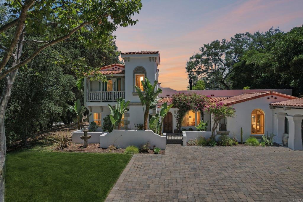 Imagine arriving at this breathtaking Spanish estate, where a heavy wrought iron & wood gate welcomes you into a world of timeless beauty & seclusion. As you wind through the driveway lined with olive & fruit orchards, you’re embraced by the canopy of majestic old oaks. Walking the grounds feels like stepping into the pages of a design magazine — every detail curated for visual charm & function. Bougainvillea cascades gracefully around the arched wooden front door, framing the entrance with vibrant color & creating a picture-perfect welcome for guests. The enchanting courtyard entry sets the tone, offers an ideal space to greet friends with the soft sounds of a bubbling fountain & the scent of lush garden blooms. Step inside, & you’re greeted by authentic Mexican pavers underfoot & rich wood-beamed ceilings overhead — every detail curated for warmth, character, & soul. A stunning arched stained glass window adds a touch of old-world artistry, casting beautiful, dappled light across the interior. The sunlit great room is anchored by a classic fireplace, & three sets of French doors open wide to the backyard, blurring the line between indoor/outdoor spaces & creating the ultimate living experience. The gourmet kitchen is a showstopper — an authentic Spanish-style space that’s anything but cookie cutter. From its arched alcove over the stove to the handcrafted tilework & oversized island, it invites you to imagine an Italian grandmother rolling fresh pasta, simmering a rich Bolognese, or baking rustic bread with love. The home is thoughtfully designed with a luxurious primary suite on the main floor, where you’ll find another set of double French doors & a stunning fireplace to warm the room & set a romantic, cozy tone. The spa-like primary bath offers a separate walk-in shower & a soaking tub — the perfect retreat for relaxing. Upstairs, a private guest suite with its own separate entrance & its own kitchenette, bath, & large living room that could also serve as an extra bedroom opens onto a spacious deck with commanding views stretching for miles — including the iconic Pu’éska mountain in the distance, sacred to the Pechanga tribe & part of the Santa Margarita Ecological Preserve. It’s a dreamy perch to savor the sunset, with panoramic views over the infinity-edge pool & spa, rolling hills & open space. Outside, the lush, tropical landscaping envelops the home, creating a private oasis around the vanishing-edge infinity pool, paver patios, & an inviting outdoor fireplace — perfect for gathering under the stars on warm summer nights. Meandering paths weave throughout, inviting you to stroll or ride as you collect your daily eggs, tend to your vegetable garden or simply enjoy the fresh air — with so much to do, you’ll never be bored. The charming outbuildings house chickens & small livestock, while a separate shaded area of old-growth trees is perfectly suited for horses, goats, or cattle. As the olive trees mature, you’ll have the opportunity to craft your own olive oil or canned olives — as a rewarding family hobby or business. Even the covered carport is a work of art, with exposed wood beams overhead adding rustic & architectural character. As you walk the grounds, you can feel the cool breeze stirring the air, wrapping you in the sense of a heritage estate where time slows & memories are made — bringing a peacefulness that’s hard to find. Behind the scenes, the property is equally impressive: a newer oversized septic system ready for a potential guest house, a 22KW Generac whole-house generator, & a 4-person electric Redwood Outdoors sauna that feels like you are enveloped in a forest. For those dreaming even bigger, an adjacent 24-acre parcel with a year-round stream is available for sale as well — offering a rare opportunity to own an expansive, secluded estate minutes from the charm of Old Town. This extraordinary estate offers not just a home, but a lifestyle — a rare blend of luxury, nature, & timeless beauty.