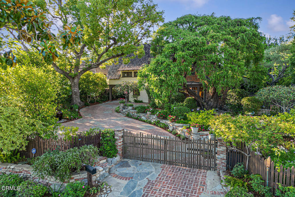 Nestled within the prestigious Oak Knoll neighborhood behind a private gate, this enchanting English Revival, designed by noted architect H. Denman Schutt, located near the renowned Langham Hotel, offers a rare blend of timeless elegance and tranquil seclusion. A storybook front garden, adorned with flagstone and vintage brick pathways, lush greenery, and a serene vase fountain, leads to a welcoming covered porch and gracious entryway. The step-down formal living room showcases gleaming peg-and-groove flooring, while a handsome fireplace, flanked by French doors, opens to a central courtyard where the gentle sound of a Batchelder-style tiled fountain creates a serene retreat. The striking leaded-glass bay window frames the idyllic views of the manicured front garden. Discreetly tucked behind a bookshelf lies a whimsical speakeasy-style bar, a nostalgic nod to a bygone era that adds a playful touch to the room's grandeur. The formal dining room is elevated by exquisite leaded windows and doors; intricate moldings, a parquet floor with inlaid 'wood rug' design and the French doors open to a romantic Porte Cochere. Adjacent is the open gourmet kitchen featuring a generous soapstone island, premium stainless steel appliances, custom cabinetry, and a sunlit breakfast nook with a view of the lush rear garden and the natural, green pool that blends in like a pond. Just off the kitchen, an intimate sitting area with a second fireplace and French doors offer seamless access to the courtyard and an inviting pathway to the enclosed pool and spa--perfect for effortless indoor-outdoor living. A stylish powder room completes the main level. Upstairs, two private suites and a spacious third bedroom offer both comfort and versatility. The front suite features an entire wall of built-in shelving and cabinetry, along with vintage leaded windows. The rear suite includes dual walk-in closets and a charming ensuite bath with double vanities and a dual-head shower. A large hall bath servicing the third bedroom features a classic pedestal sink and soaking tub, plus a convenient laundry closet, round out the upper level. The detached two-car garage is topped by a versatile bonus room--ideal as a home office or gym. Additional highlights include rich wood flooring throughout, fresh interior paint, and upgraded attic insulation. Framed by romantic gardens, meandering walkways, multiple fountains, and a whimsical pond, this magical home is ready to welcome its next fortun