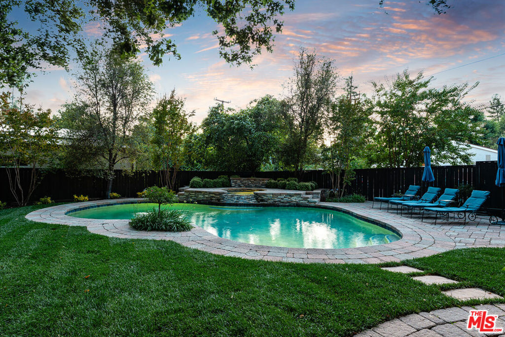 A river runs through it - literally. Welcome to 23040 Blue Bird Drive, a one-of-a-kind retreat in one of Calabasas' most beloved and historic neighborhoods: the Bird Streets. This custom-built home is not only one of the newest and largest in the community, but it's also hitting the market for the very first time, offered by its original owners who have lovingly maintained and thoughtfully updated the property over time. Set on a generous corner lot - larger than most in the Bird Streets - and wrapped on three sides by Belgard pavers and custom hardscaping, the home offers two separate backyard zones, stunning neighbor separation, and a rare feeling of expansiveness. Mature coastal oaks and gorgeous Japanese maples create an organic canopy over the grounds, and a creek running through the backyard adds a truly magical, storybook quality to the setting. With its high ceilings throughout, open floor plan, and walls of windows framing treetop views, the home evokes the feeling of a modern treehouse - quietly tucked away yet just minutes from everything Calabasas has to offer. Whether you're sipping coffee on the deck or crossing the private bridge to your personal backyard "island," every space in this home invites a slower pace and intentional living. Inside, the layout is both elegant and functional. A formal dining room sits off the airy entryway, while a formal living room with walk-in closet and adjacent full bath offers EASY CONVERSION TO A FOURTH BEDROOM or flexible guest space. The expansive family room centers around a cozy fireplace and opens directly to the rear deck - ideal for effortless indoor-outdoor entertaining. The adjacent kitchen is light-filled and welcoming, with a granite island and prep sink, charming bay window, casual dining area, and a butler's pantry with second sink - perfect for everyday function or holiday hosting. Upstairs, the primary suite feels like a private wooded retreat, with a peaceful balcony, two walk-in closets, a large attached sitting room with its own fireplace, and an expansive ensuite bath featuring travertine floors, soaking tub, separate vanities/makeup counter, and large picture windows that invite the outdoors in. Two additional bedrooms are spacious and have en-suite baths, while a custom built-in office on the upper landing offers flexibility as a work area, study zone, or relaxing hideaway. The outdoor space is as thoughtful as it is serene. The fully enclosed backyard includes new fencing, a sparkling pool with elevated waterfall spa, manicured lawns, Zen-style seating areas, and abundant landscaping - all designed to blend seamlessly with the natural surroundings. Perfectly situated in a warm, established community, this is your chance to own a rare slice of Calabasas history - a home where scale, privacy, character, and nature converge. If you've been searching for a place that's truly set apart yet deeply connected to the lifestyle you love, 23040 Blue Bird Drive is ready to welcome you home.