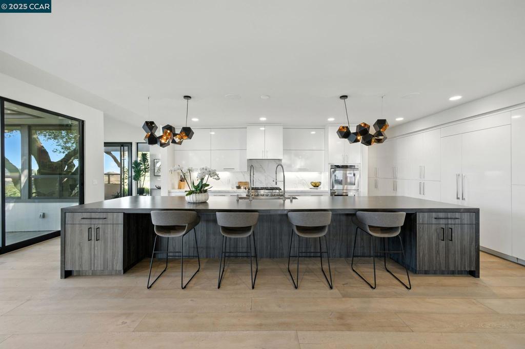 This modernist retreat, rebuilt from the studs in 2019, is set on a private lane just a mile from top-rated Sleepy Hollow School. It offers architectural distinction and a seamless connection to nature, with views of Briones and the hillsides beyond. Mature trees surround manicured gardens and a grassy play area. The open-concept kitchen (with elite appliances) and dining room sit under elevated ceilings. A waterfall island, nearly 80 sq ft, provides bar seating for 5, and the adjacent dining room seats 10–12. A glass wine cellar showcases 180 bottles. Sliders open directly to the deck, where gas heaters ensure year-round comfort. The living room offers a sleek fireplace and oversized windows. The office near the entry hall makes work from home easy. (The room could be reconfigured as a nursery or 5th bedroom.) The principal suite offers 2 private decks and a bathroom featuring Porcelanosa tile, marble floors, dual vanities, an oversized shower and panoramic outlooks. The closet accommodates any wardrobe. Two more bedroom/bathrooms are upstairs. Between them lies the movie studio, certain to be the gathering place for entertainment of family and guests. The 4th bedroom suite, downstairs, is accessed by a private entrance and is ideal for an au pair, in-laws, or guests.