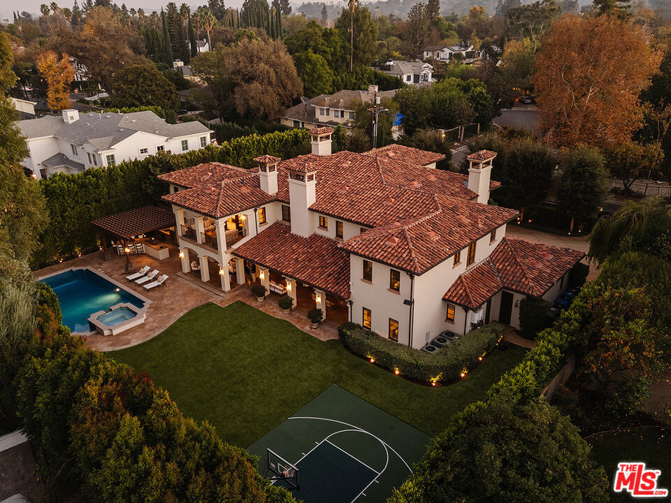 Built by the renowned AMG Group, this ultra-private, gated home is located in the highly sought-after Amestoy Estates neighborhood. Meticulously designed with every detail in mind, the property offers an unparalleled blend of luxury, sophistication, and privacy. A grand circular driveway with dual two-car garages leads you to this exquisite estate, where a high-end security system ensures peace of mind. The home's striking architecture is enhanced by Venetian plaster finishes and rich hardwood floors, including elegant Parquet flooring that adds warmth and texture throughout the living spaces. The home has six bedrooms plus an office and separate gym. Five fireplaces create a sense of ambiance, whether in the large formal living room, the cozy family room, or the luxurious primary suite. The open and airy layout features expansive living and dining rooms, perfect for both formal and casual gatherings. The family room flows seamlessly into the gourmet chef's kitchen, a true culinary masterpiece. The kitchen boasts a large center island with dual sinks, dual dishwashers, a six-burner range, double convection ovens, a warming drawer, and a steamer, everything a discerning chef could desire. The adjacent butler's pantry features extra refrigeration, a dual freezer, and a wine refrigerator for added convenience. The kitchen opens to the backyard through French doors with retractable screens, creating an ideal indoor-outdoor living experience. Upstairs, you'll find four luxurious ensuite bedrooms, each thoughtfully designed with ample closet space and private bathrooms. The spacious second-family room, located near the bedrooms, provides a perfect retreat or additional living space. A well-appointed laundry room with dual washers and dryers adds convenience to daily living. The primary suite is a true sanctuary. The generous space includes a sitting area with fireplace, three walk-in closets, and a private balcony that offers sweeping views of the estate. The lavish primary bath is a retreat in itself, featuring dual water closets, a steam shower, and a spa tub. No detail has been overlooked, creating a serene and indulgent experience. The home offers two additional ensuite bedrooms on the main level, perfect for guests or family. A custom-built office with rich wood detailing creates a quiet and sophisticated space for work or study. The expansive backyard is an entertainer's dream. A custom-tiled pool and spa set the tone for relaxation, while the covered patio with wood-burning fireplace provides a perfect space for al fresco dining or lounging. The pergola-covered outdoor kitchen is equipped with a BBQ, smoker oven, sink, and gas burners, offering everything needed for a gourmet outdoor experience. A sports court adds an active element to the outdoor space, ensuring there's something for everyone to enjoy. Whether you're relaxing by the pool, entertaining guests on the spacious patio, or enjoying a quiet moment in the privacy of your own primary suite, this estate offers a rare combination of timeless elegance and modern convenience. The seamless flow between indoor and outdoor spaces, luxurious finishes, and thoughtful design elements make this home the ultimate in high-end living.
