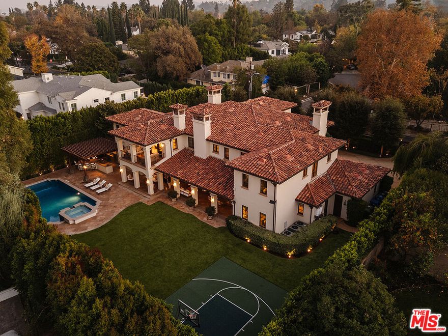 Built by the renowned AMG Group, this ultra-private, gated home is located in the highly sought-after Amestoy Estates neighborhood. Meticulously designed with every detail in mind, the property offers an unparalleled blend of luxury, sophistication, and privacy. A grand circular driveway with dual two-car garages leads you to this exquisite estate, where a high-end security system ensures peace of mind. The home's striking architecture is enhanced by Venetian plaster finishes and rich hardwood floors, including elegant Parquet flooring that adds warmth and texture throughout the living spaces. The home has six bedrooms plus an office and separate gym. Five fireplaces create a sense of ambiance, whether in the large formal living room, the cozy family room, or the luxurious primary suite. The open and airy layout features expansive living and dining rooms, perfect for both formal and casual gatherings. The family room flows seamlessly into the gourmet chef's kitchen, a true culinary masterpiece. The kitchen boasts a large center island with dual sinks, dual dishwashers, a six-burner range, double convection ovens, a warming drawer, and a steamer, everything a discerning chef could desire. The adjacent butler's pantry features extra refrigeration, a dual freezer, and a wine refrigerator for added convenience. The kitchen opens to the backyard through French doors with retractable screens, creating an ideal indoor-outdoor living experience. Upstairs, you'll find four luxurious ensuite bedrooms, each thoughtfully designed with ample closet space and private bathrooms. The spacious second-family room, located near the bedrooms, provides a perfect retreat or additional living space. A well-appointed laundry room with dual washers and dryers adds convenience to daily living. The primary suite is a true sanctuary. The generous space includes a sitting area with fireplace, three walk-in closets, and a private balcony that offers sweeping views of the estate. The lavish primary bath is a retreat in itself, featuring dual water closets, a steam shower, and a spa tub. No detail has been overlooked, creating a serene and indulgent experience. The home offers two additional ensuite bedrooms on the main level, perfect for guests or family. A custom-built office with rich wood detailing creates a quiet and sophisticated space for work or study. The expansive backyard is an entertainer's dream. A custom-tiled pool and spa set the tone for relaxation, while the covered patio with wood-burning fireplace provides a perfect space for al fresco dining or lounging. The pergola-covered outdoor kitchen is equipped with a BBQ, smoker oven, sink, and gas burners, offering everything needed for a gourmet outdoor experience. A sports court adds an active element to the outdoor space, ensuring there's something for everyone to enjoy. Whether you're relaxing by the pool, entertaining guests on the spacious patio, or enjoying a quiet moment in the privacy of your own primary suite, this estate offers a rare combination of timeless elegance and modern convenience. The seamless flow between indoor and outdoor spaces, luxurious finishes, and thoughtful design elements make this home the ultimate in high-end living.