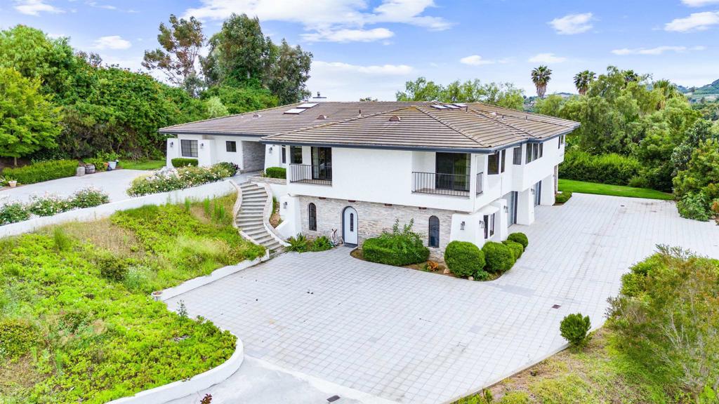 Welcome to an extraordinary lifestyle in Fallbrook's prestigious Rolling Hills gated community, offering privacy and security with 24-hour guard service. Enter through beautifully landscaped grounds featuring tranquil water features and lush park-like settings. Enjoy access to the clubhouse and tennis courts amid rolling hillsides. This impeccably modernized estate sits on 2.65 fully fenced acres, perfect for gatherings and includes a sprawling orchard of avocados and fruit trees, irrigated mainly by a well with a new pump, filter, motor, and reservoirs installed in 2023. Step inside to a formal entry and living room with cathedral-beam ceilings, a sleek linear fireplace, and abundant natural light from skylights. The gourmet kitchen boasts Viking appliances, a grey quartz island, white quartz countertops, a walk-in pantry, and a breakfast area opening to the patio. All secondary bathrooms are newly remodeled with a fresh modern look; the guest bath features a charming retro-modern style. The primary bathroom is fully transformed with a large walk-in shower, oversized rain showerhead, and a luxurious soaking tub. A water softener was installed in 2021. The spacious primary suite includes a private deck with panoramic views. Two additional bedroom suites each have full baths and deck access overlooking the grove. The living room opens to a game room, ideal for entertaining. A new elevator (2024) connects the main level to the oversized 4-car garage with insulated stainless steel doors and ample storage. An attached 500 sq ft ADU with a kitchenette, exterior entrance, and parking adds versatility. Dual A/C and heating systems ensure comfort year-round. Exterior stucco repairs and paint were completed in March 2023. Owned solar panels installed in 2019 provide energy efficiency. Live in one of Fallbrook’s most sought-after neighborhoods, close to new wineries, restaurants, golf courses, and just a short drive to beaches and vibrant entertainment. Don’t miss this magnificent estate—contact us today to schedule your private tour.