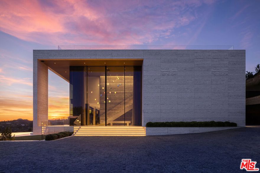 Commanding one of the most coveted promontories on the Westside, this architectural tour de force by Thomas Juul-Hansen unfolds across two acres, framing sweeping vistas from downtown to the Pacific. Clad in Alabastrino Travertinethe same stone that graces the neighboring Getty Museum the residence strikes a perfect balance between modern design and natural warmth, with rich wood paneling and sculptural slatting adding depth and character to its expansive spaces. Designed for both grand entertaining and intimate living, the home's fluid layout and soaring volume is anchored by a striking formal living room, where sky-high pocket glass doors erase the boundary between indoors and out, revealing an uninterrupted panorama of city lights and ocean horizons. The dining room and chef's kitchen, both equally breathtaking, extend this effortless openness, blending refinement with functionality. The primary suite is a private sanctuary, enveloped in glass and spilling onto wraparound terraces that offer unobstructed views in every direction. Additional guest suites, each generously scaled, echo this same ethos of light, openness, and connection to the landscape. Elevated amenities abound a state-of-the-art home theater, fitness and wellness studio, and a meticulously curated wine cellar ensuring every element of modern luxury is accounted for. Beyond the walls of glass, the estate unfolds into an expansive outdoor retreat. A sprawling patio and flat grassy lawn lead to a showstopping infinity-edge pool and spa, seamlessly merging with the horizon. An outdoor kitchen, built-in BBQ, and a rooftop terrace unlike any other in Los Angeles provide the ultimate setting for both large-scale hosting and private sunset escapes. A masterclass in design, craftsmanship, and setting, this estate is more than a home it's a legacy, an architectural landmark poised above the city, offering an unparalleled fusion of privacy, scale, and world-class design.