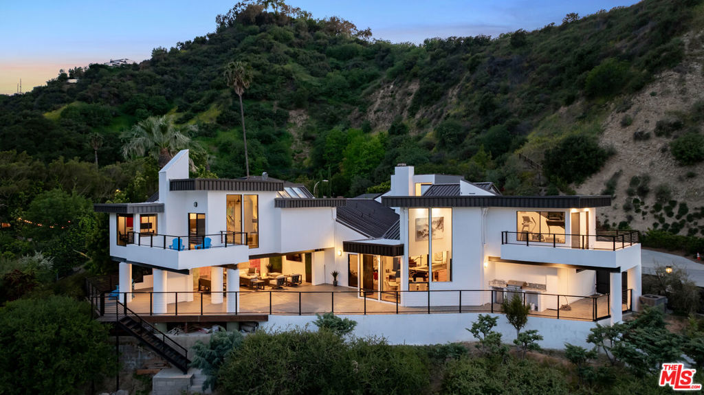 Perched above it all at the end of a quiet cul-de-sac in Longridge Estates, this one-of-a-kind Marshall Lewis designed architectural is a true retreat. Set on a full acre with sweeping jetliner views of the San Fernando Valley from nearly every room, this ultra-private 5-bed, 3.5 bath split-level blends nature, privacy, and that all important indoor-outdoor Iiving. Inside, hand-distressed hardwood floors, vaulted ceilings, a revamped Nest-controlled HVAC system, and tons of natural light create a space that feels both grounded and elevated. The open layout flows effortlessly from the dramatic living room to a sunny sitting room with wraparound windows that frame the mountains, canyons, and city lights like art. The formal dining area opens to a large view deck perfect for entertaining. The kitchen is smart and cheerful with stainless steel appliances and a breakfast room, while upstairs, the expansive primary suite is its own sanctuary with a fireplace, sitting area, and oversized balcony with panoramic sunrise views.