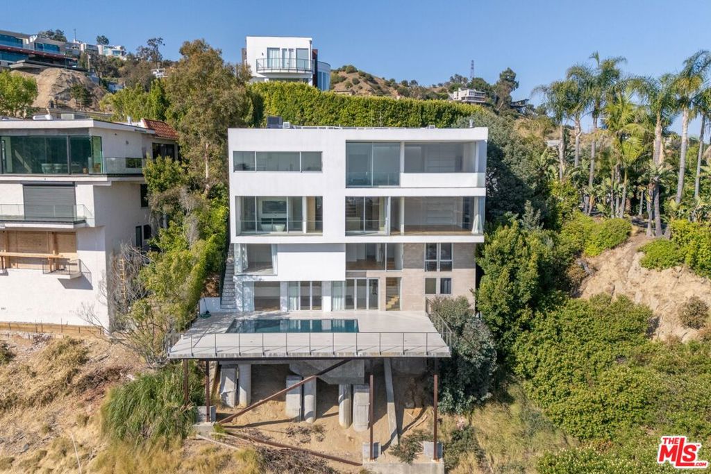 Perched above the city with unobstructed panoramic views from Downtown Los Angeles to the Pacific Ocean and Catalina Island, this contemporary masterpiece defines elevated living. Located just moments from the iconic Sunset Boulevard, the home offers the rare combination of architectural distinction, refined design, and everyday comfort.With 4 spacious bedrooms and 6 elegantly appointed bathrooms, the layout is designed for both grand entertaining and relaxed day-to-day living. The oversized primary suite is a true sanctuary featuring dramatic floor-to-ceiling glass that captures breathtaking views, two luxurious full bathrooms, a large custom walk-in closet, and a private balcony perfect for morning coffee or sunset wind-downs.At the heart of the home, a stunning Boffi kitchen is outfitted with top-of-the-line Miele and Wolf appliances, ideal for hosting with both style and ease. The open-concept living areas flow seamlessly to the expansive pool deck, where sweeping city-to-ocean views set the stage for unforgettable entertaining or quiet relaxation under the stars.Additional highlights include a custom wine cellar, a spa-like steam shower, and smart home features such as Dom Vision automation, in-wall iPads, built-in surround sound, electronic shades, and sleek Boffi vanities and fixtures throughout.Whether you're hosting a lively soire or enjoying a private moment with the skyline, this home offers a lifestyle that's as luxurious as it is livable.
