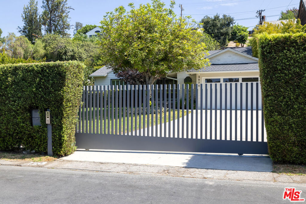Hedged for privacy and secured by a motorized modern gate, this 3-bedroom, 2-bath Studio City home offers a rare combination of style, comfort, and location. A grassy front yard framed by a mature shade tree sets the tone for the warm interiors. Oak wood floors flow through the living spaces, where a double-sided fireplace connects the living room and expansive family room. The designer kitchen features marble counters, custom cabinetry, and an eat-in dining area, while the formal dining room is elevated with bespoke wallpaper and a striking partition sliding wall. Bedrooms are outfitted with wood shutters, tailored window treatments, and upgraded closet hardware, while the third bedroom doubles as a quiet home office with built-in drawers. The family room opens to a lush, private backyard retreat complete with built-in stainless BBQ and inviting spaideal for relaxation or entertaining. Just steps from the open-air Shops at Sportsmen's Lodge, enjoy Erewhon, Equinox, Civil Coffee, Sugarfish, and the hidden gem Cosette Wine Bar. Located in one of LA's most sought-after neighborhoods, long favored by celebrities and industry insiders, this residence pairs refined finishes with an unbeatable address.
