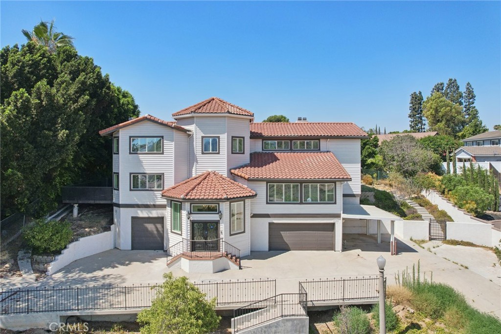 Experience the perfect blend of privacy, elegance, and luxury in this turn key, one-of-a-kind Yorba Linda estate, tucked away at the end of a peaceful cul-de-sac on a private road shared with only three neighbors. A long, dramatic driveway leads to a grand foyer with a sweeping three-story spiral staircase, setting the tone for the sophisticated living spaces that follow. The open, light-filled layout is perfect for entertaining, featuring a spacious living room with vaulted ceilings, a formal dining room bathed in natural light, and an expansive entertainment room complete with a wet bar, mini-fridge, wine storage, fireplace, and space for gatherings of any size. The gourmet kitchen offers recessed lighting, floor-to-ceiling cabinetry, abundant counter space, and a walk-in pantry, with a breakfast nook and family room opening to an elevated deck ideal for dining under the stars. The luxurious primary suite features vaulted ceilings, a private balcony, fireplace, spa-inspired bath, and two oversized walk-in closets. Additional bedrooms share balconies and a Jack-and-Jill bath. Parking and storage are exceptional with an oversized two-car garage with built-ins, a second oversized garage with half bath and tall ceilings for larger vehicles, plus a covered carport. The backyard is a private retreat with a pool, spa, fountain, and elevated deck, complemented by a large hobby room for creative projects. Set on a half-acre hill with mountain views, mature trees, and fruit trees, this rare property offers the ultimate in seclusion while being just minutes from Imperial Highway and the 91 Freeway—an incredible opportunity to own your estate in one of Yorba Linda’s most desirable locations.