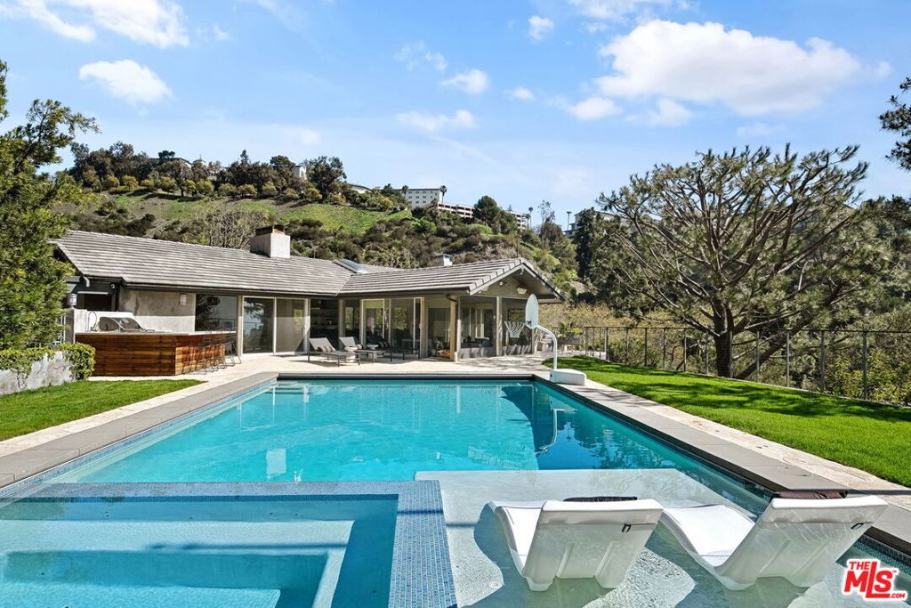 Perched above Sunset Boulevard, this reimagined Brentwood estate offers a rare balance of serenity and sophistication. Set on over an acre of grounds, the residence unfolds across nearly 6,000 sq ft with 6 bedrooms and 7 baths, all enhanced by a 2012 renovation that introduced modern finishes and an airy open plan. Floor-to-ceiling windows frame lush hillside vistas, while light-filled interiors showcase contemporary fireplaces and seamless indoor-outdoor living. The chef's kitchen, designed with quartz counters, custom cabinetry, and premium appliances, anchors the home with both beauty and function.Tailored for entertaining, the estate features a sleek indoor bar, a private theater with convertible guest suite, and an expansive backyard retreat complete with resort pool, cabana, outdoor kitchen, and professional putting green. Smart technology and thoughtful upgrades including solar power, EV charging, a natural gas generator, and water filtration add ease to everyday living. A true sanctuary in one of Los Angeles' most prestigious neighborhoods.