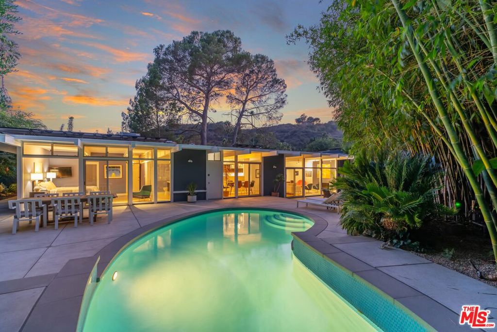 Tucked away at the end of a cul-de-sac in coveted Upper Nichols Canyon Colony, this post-and-beam jewel is more than a home-it is a living work of art. Originally crafted in 1959 by Modern Trend Construction Co., whose collaborations included celebrated architects Richard Dorman and Edward Fickett, this residence is part of the storied "Hollywood Highlands" enclave- a midcentury architectural neighborhood of wide streets, sidewalks, and clean lines unobstructed by power poles. From the moment you step inside, natural light and architectural detail define the experience. A skylit entryway frames sweeping views of Briar Summit Open Space Preserve, inviting you deeper into the home. The generous foyer leads into a dramatic and spacious living room, where floor-to-ceiling windows create a luminous backdrop of sky, patio, and pool. Walls of glass span the rear facade, dissolving the boundary between indoors and outdoors and embodying the quintessential Southern California lifestyle. The main living spaces flow effortlessly- living, dining, and primary suite all open to the private pool and terrace. The primary suite is a serene retreat, complete with clerestory windows, a walk-in closet, and sliding doors to the patio and pool. Its en-suite bath mirrors the architectural rhythm, with windows that usher in natural light, enhanced by automated shades that provide privacy at the touch of a button. The flexible floor plan includes a bedroom opened to create a den/office, easily restorable to a private bedroom if desired. A third bedroom has sliding glass doors to a private patio and garden retreat. Modern upgrades blend seamlessly with midcentury character: Solar panels, solar pool heating, an EV charger, a whole-home backup generator, new HVAC (2024), new porcelain tile flooring (2025), and a recently replaced roof and garage door. Outdoors, enjoy a secluded oasis shaded by mature landscaping and prolific grapefruit and peach trees- alongside the sparkling pool, a natural extension of the home's indoor-outdoor design. Centrally located just off Mulholland Drive, this rare architectural offering places you minutes from Studio City, Hollywood, and Burbank's studios, while maintaining a sense of retreat and privacy. This is not simply a residence. It is an emblem of midcentury modern design- an architectural statement, preserved and refined for contemporary living.