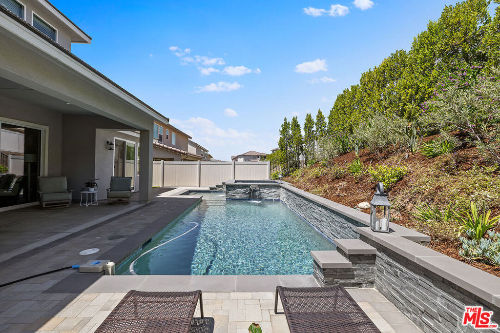 Luxury Living with a PRIVATE WATERFALL POOL in Santa Clarita's Premier Skyline Community. Don't miss this rare opportunity to own a nearly-new luxury residence built in 2023, now available at an incredible new price! This 4-bedroom + office + loft, 2.5-bathroom home is the epitome of modern sophistication, comfort, and smart design located in one of Santa Clarita's most desirable neighborhoods. Key Highlights: PRIVATE Zen-Inspired Backyard Oasis with custom WATERFALL POOL, rejuvenating hot tub, built-in outdoor kitchen, and lush, privacy-focused landscaping; FIRST FLOOR PRIMARY SUITE with spa-like ensuite, walk-in closet, and private backyard access; Chef's Kitchen with stainless steel appliances, quartz countertops, dark shaker cabinets, walk-in pantry & oversized island; Open-Concept Great Room with elegant dining space, family room, and CUSTOM BUILT-IN CABINETRY & BAR SHELVING; Dedicated Office + Versatile Loft ideal for a second workspace, media room, or lounge; Energy-efficient living with OWNED SOLAR and Fire Suppression Sprinkler System; Designer touches throughout including soaring ceilings, dramatic iron staircase, and premium finishes. Built for Comfort & Entertainment; Whether you're hosting a sunset dinner by the pool or enjoying a cozy night in, this home adapts beautifully to your lifestyle. The seamless flow from indoors to outdoors creates the perfect setting for both quiet relaxation and memorable gatherings. Skyline Community Perks: Enjoy resort-style amenities including a modern fitness center, scenic paseos, sparkling community pool, clubhouse, and more all nestled in a picturesque and peaceful setting just minutes from shops, dining, and top-rated schools. ACT NOW - THIS HOME WON'T LAST LONG AT THIS PRICE!