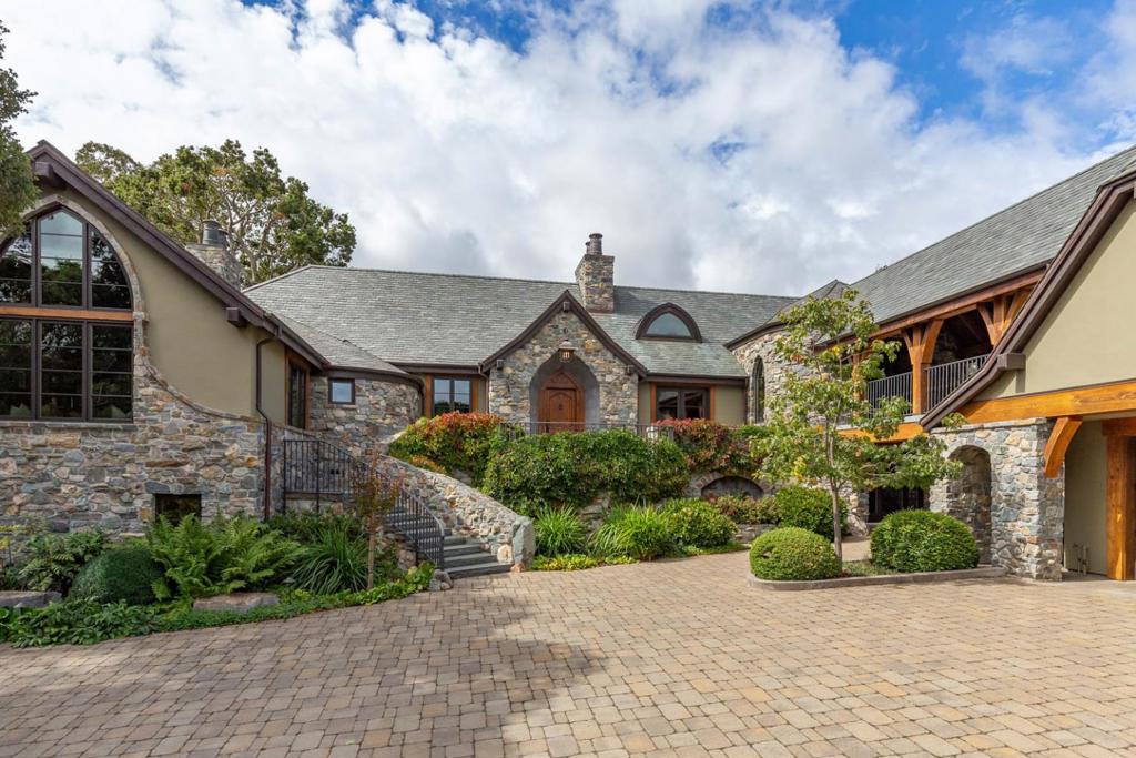 Set on two acres of picturesque rolling hills dotted with California oaks, this country manor is architecturally designed to evoke the beauty & appeal of a French country estate. Inside & out, the home embodies elegance & charm with rustic sophistication. The exterior is a harmonious blend of natural stone & stucco siding, complemented by a high-pitched Vermont slate roof. Large arched windows & handcrafted oak timber doors enhance the sense of history & authenticity. The design features a masterfully constructed covered bridge, made from reclaimed barn wood & bluestone flooring, connecting the round turret of the main home to the upper-level guest quarters above one of two garages. Handcrafted wrought iron railings, skillfully forged by a blacksmith, adorn the bridge, the front porch, & stairways from the motor court, adding artistic detail at every corner. Home exudes rustic grandeur with lofty ceilings constructed from hand-hewn century-old beam timbers. Located just minutes from the heart of Silicon Valley, this country manor harmoniously blends architectural splendor, natural beauty, & modern conveniences. It stands as a testament to refined living, where the allure of the past meets the dynamism of the present, creating a sanctuary that is both timeless and contemporary.