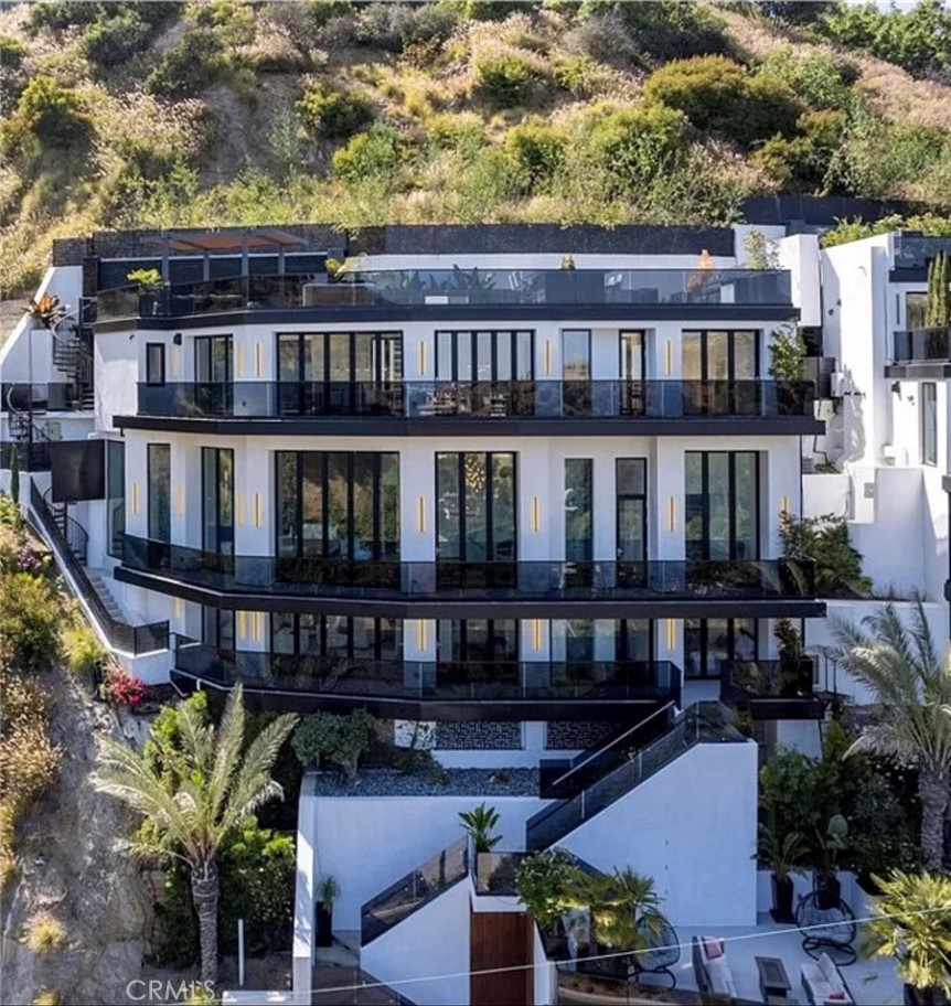 Set high above the city in one of L.A.’s most iconic neighborhoods, 8148 Gould Ave offers a rare blend of modern design, privacy, and panoramic beauty. This newly constructed 4-bedroom, 6-bathroom residence redefines what it means to live well in the Hollywood Hills — with expansive living areas, flexible floorplans, and outdoor spaces that invite connection, relaxation, and escape. The top floor features an open-concept kitchen, dining area, and living room that opens to a terrace and two-story waterfall feeding into a heated pool, spa, and cedar sauna. Above, a rooftop deck offers a built-in BBQ, hot tub, and lounge space with iconic views. The primary suite level is a luxurious escape with 14-foot ceilings, a fireplace, a spa-inspired bathroom, and a 30-foot custom closet. A second ensuite bedroom with terrace access makes an ideal guest space or office. The lower level functions as a fully equipped 2-bed, 2-bath guest suite with its own kitchen, laundry, private patio, and hidden wine cellar — perfect for extended stays or added privacy. A commercial-grade elevator connects all levels to the street-level garage with EV charging.