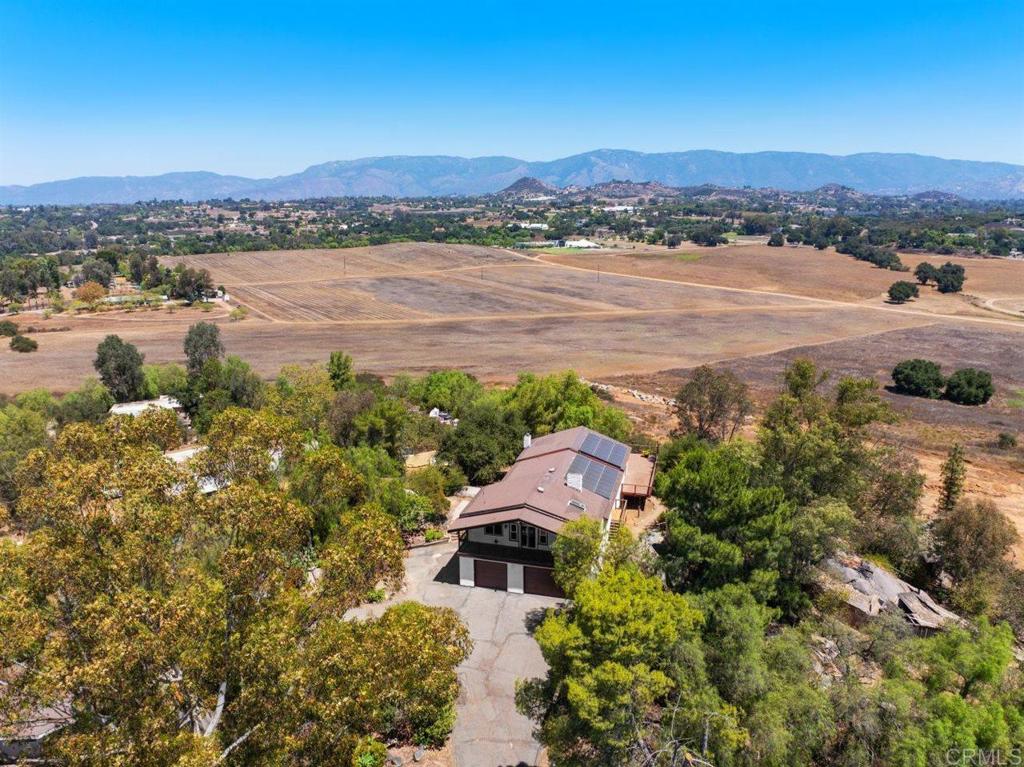 Perched on 2.08 acres with jaw dropping panoramic views of Palomar Mountain and Valley Center’s rolling hills, this unique and extensively renovated split-level property offers space, privacy, and charm in every direction. From the gated circular drive, you will find a blend of modern updates and timeless country character. Freshly painted inside and out, the home features new luxury vinyl plank flooring throughout, updated ceiling fans, a modern new spiral staircase railing, and so much more! The main level’s freshly painted light and bright vaulted open-beam ceilings and dramatic great room look out to WOW views and set the stage for everything from cozy nights by the wood-burning fireplace to lively gatherings. The entertainer’s kitchen features granite counters, an oversized island with cooktop, a walk-in pantry, and ample cabinetry. The dining area opens to an expansive, zero-maintenance EON wrap-around deck where you can enjoy breathtaking sunsets and starlit skies. The primary suite includes a brick fireplace, private balcony, and a spa-like bath with a freestanding tub. The extensively renovated lower-level bedroom and living space offers endless possibilities for a gym, guest suite, multi-generational living. Outdoors offers a playground for all ages; wander winding paths through lush landscaping, explore the unique whimsical replica western mine, or garden in the fenced vegetable beds. Pipe corrals are ready for horses, and a versatile outbuilding can serve as a workshop, art studio, office, playroom or whatever you can envision! Additional features include an attached 3-car garage with built-in cabinets and workbenches, leased solar ($303/mo), and no HOA! Truly an enchanting property not to miss!