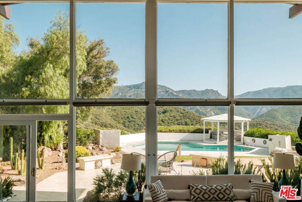 A Premiere Mid-Century Modern Haven with Unrivaled Views "Open one's world to the environment," proclaimed Austrian master architect Rudolf Schindler, an ethos fully realized in this exhilarating glass-walled estate. Perched on a private promontory in the Santa Monica Mountains, the residence commands sweeping canyon and mountain panoramas from every room, marrying iconic Mid-Century architecture with contemporary luxury. Step through grand double doors into a soaring, light-filled interior where the indoors and outdoors blend in perfect harmony. A newly re-imagined, chef-caliber kitchen cascades into the dramatic living room, its statement fireplace anchoring lofty ceilings and an airy open plan. Walls of glass unveil expansive wrap-around decks ideal for al-fresco soirees or a quiet sunset toast. Beyond, manicured grounds reveal a custom-designed swimming pool, shaded gazebo, and terraced gardens that frame jaw-dropping vistas at every turn. Sunrise bathes the home in golden light; ocean breezes drift up from Malibu by day; vibrant sunsets paint the horizon each evening. Tucked up a discreet private drive, this sanctuary offers instant access to pristine beaches, world-class hiking and equestrian trails, celebrated dining, and the coveted Las Virgenes school district yet feels worlds away from it all. For those seeking premier design, soulful serenity, and an effortless indoor-outdoor lifestyle, this Modern Mid-Century masterpiece is where luxury meets nature in its purest form.