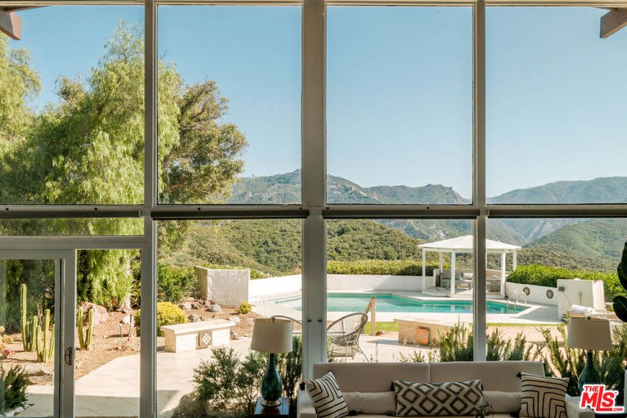 A Premiere Mid-Century Modern Haven with Unrivaled Views "Open one's world to the environment," proclaimed Austrian master architect Rudolf Schindler, an ethos fully realized in this exhilarating glass-walled estate. Perched on a private promontory in the Santa Monica Mountains, the residence commands sweeping canyon and mountain panoramas from every room, marrying iconic Mid-Century architecture with contemporary luxury. Step through grand double doors into a soaring, light-filled interior where the indoors and outdoors blend in perfect harmony. A newly re-imagined, chef-caliber kitchen cascades into the dramatic living room, its statement fireplace anchoring lofty ceilings and an airy open plan. Walls of glass unveil expansive wrap-around decks ideal for al-fresco soirees or a quiet sunset toast. Beyond, manicured grounds reveal a custom-designed swimming pool, shaded gazebo, and terraced gardens that frame jaw-dropping vistas at every turn. Sunrise bathes the home in golden light; ocean breezes drift up from Malibu by day; vibrant sunsets paint the horizon each evening. Tucked up a discreet private drive, this sanctuary offers instant access to pristine beaches, Direct access to world-class hiking and equestrian trails, celebrated dining, and the coveted Las Virgenes school district yet feels worlds away from it all. For those seeking premier design, soulful serenity, and an effortless indoor-outdoor lifestyle, this Modern Mid-Century masterpiece is where luxury meets nature in its purest form.