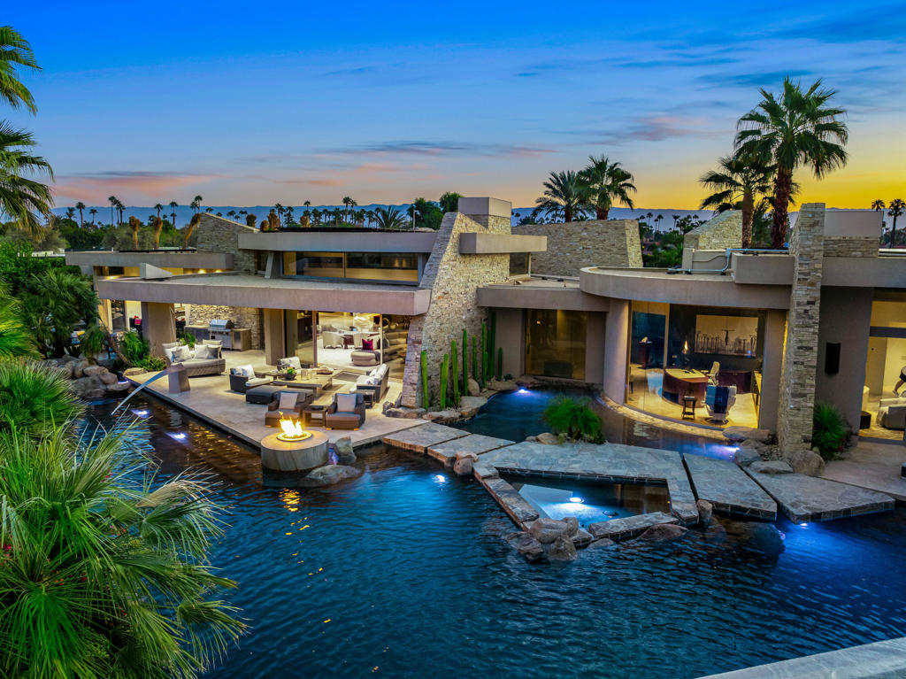 Stunning Guy Drier architectural masterpiece in the heart of Rancho Mirage. This 10,019 SF, privately gated compound is situated on 2 acres, and features the finest in indoor/outdoor living. The main house has a expansive primary wing, with two luxurious master baths, washer and dryer and generous walk-in closets and an executive office. There are also three guest suites, with access to the backyard. There is also a next level self-contained guest house that features a formal living room, full kitchen + catering kitchen, laundry room, guest suite, gym and a huge covered patio. Amenities also include a resort worthy pool/entertaining area, championship tennis court with pavilion, bocce ball court and a putting green. This property also features Smart home automation, state of the art security system with cameras, and extensive solar system. Offered furnished per inventory