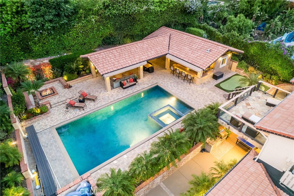Are you the go-to host for every holiday, BBQ, and Sunday game day? If you've been dreaming of a home that feels like a private resort and the "go-to" place everyone wants to be, welcome to your forever home. Tucked into the heart of North Tustin, this sprawling 5-bedroom, 5-bathroom estate sits on half an acre of lushly landscaped paradise. The showstopper? A jaw-dropping backyard designed for next-level entertaining. Whether you’re throwing a summer soirée or a winter gathering, this outdoor space adapts to every season and occasion. Dive into the oversized saltwater pool and spa, enhanced by cascading water features. The automated pool cover keeps the temperature warm year-round—pool parties in December. Unwind in one of the multiple covered patio areas, each with automatic canopies for shade, outdoor fans, and ceiling heaters for cooler evenings. Grill like a pro with two high-end stainless-steel BBQs in your fully equipped outdoor kitchen—complete with a fridge, freestanding freezer and sink. Sports fans can catch every game under the stars with outdoor TVs and smart built-in audio system surround. The pool house has a full bathroom and lounge area- you could practically live in your backyard. Inside, the magic continues. The partially open galley kitchen offers prep space and casual dining with views of the front yard. The layout flows effortlessly into the formal dining area and cozy family room, both with easy access to the backyard’s covered lounge area. The main level includes three spacious bedrooms and a home theater. Above the main level, an expansive primary retreat that opens directly to the backyard. Your spa-like ensuite has dual vanities, a walk-in shower, sunken tub, and generous his-and-hers closets. For those who want to fine-tune their short game, you’ll find putting greens in the front and in the backyard. Car lovers will appreciate the 3-car garage, which includes a car lift and dedicated workshop space. There’s also parking fo an RV, boat, or visiting guests.The entire home is powered by SmartThings technology, allowing you to control lighting, security, pool functions, irrigation, gate access, and more from your phone or remote. Everything is less than 7 years old, and the home is solar-ready with a power wall already in place—just add panels. This is more than a home—it’s a lifestyle. If you're looking for a one-of-a-kind property that turns every weekend into a vacation and makes entertaining effortless, you’ve arrived!
