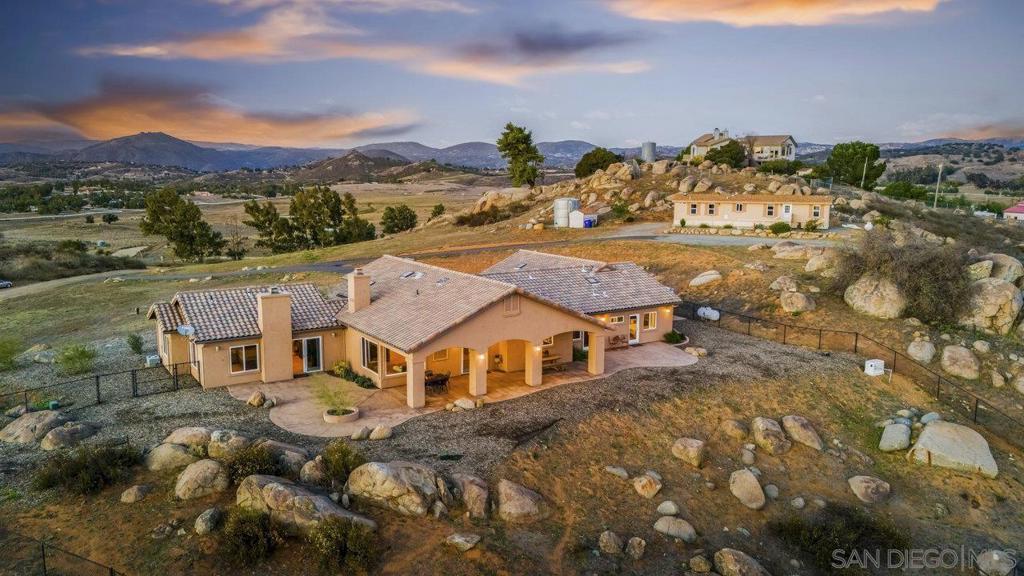 Come discover the perfect blend of refined country living and natural beauty on this exceptional 10.28-acre estate in the heart of Ramona’s sought-after wine country. Thoughtfully designed with comfort and elegance in mind, the main residence welcomes you with wide hallways, expansive picture windows, and 14 skylights that flood the home with warm, natural light. Step inside to experience the relaxed sophistication of tumbled travertine flooring, knotty alder cabinetry, granite countertops, and stainless-steel appliances—including a 5-burner gas cooktop with a custom hood. Cozy fireplaces in both the living room and the primary suite create inviting spaces to unwind and enjoy the tranquil surroundings. A highlight of the property is its equestrian setup, featuring a 6-stall barn with a 12x12 tack room and its own bathroom, a 90-foot round pen, and fully fenced and cross-fenced pastures. You’ll appreciate the 60 owned solar panels providing energy efficiency and sustainability. This property includes a 2-bedroom, 2-bath guest house/ADU—ideal for guests, multigenerational living, or a caretaker. Other features include a Generac backup generator, a high-producing well, an oversized 3-car garage and full RV hookups offer convenience for travel lovers or visiting guests. This is a true gem you don't want to miss. Schedule a viewing today.