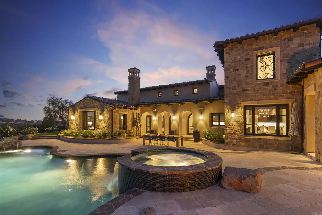 Set within the gates of Santaluz—one of San Diego's most coveted guard-gated country club communities—this 7,311 sq. ft. estate offers a rare blend of architectural elegance, thoughtful upgrades, and resort-inspired living. Positioned along the 13th green, with expansive golf course views, the residence captures a serene sense of privacy while embracing the natural beauty of its surroundings. Designed by Steve Murcko & Associates, the European-inspired estate reflects luxurious architectural attention to detail, from soaring vaulted ceilings to striking groin vault accents, complemented by arched doorways, custom built-ins, and designer stone finishes that create both intrigue and a welcoming atmosphere . Interiors unfold with a seamless flow, equally suited for intimate gatherings and large-scale entertaining, with multiple fireplaces, a wine cellar, a billiards room with wet bar, state-of-the-art theatre and a Savant whole-home entertainment system setting the stage for everyday living and celebration alike. At the heart of the home, the recently remodeled kitchen combines custom cabinetry with Taj Mahal quartzite countertops and professional-grade appliances, anchored by an oversized island, butler’s pantry, and sunlit breakfast nook. 5+ bedrooms and 5 full/2 half baths, including a primary suite with marble finishes, heated floors, dual closets, and a fireplace, provide comfort and retreat for family and guests. Expansive patios open to a private backyard oasis with a saltwater pool and spa, outdoor fireplace, barbecue kitchen, and fruit tree grove, all framed by lush landscaping and golf course views. Thoughtful upgrades such as a fully owned 23kW solar array and whole-home reverse osmosis system reflect a commitment to both luxury and sustainability. 7795 Sendero Angelica is more than a residence—it is a sanctuary, a gathering place, and a legacy estate within one of San Diego’s most celebrated guard-gated country club communities.