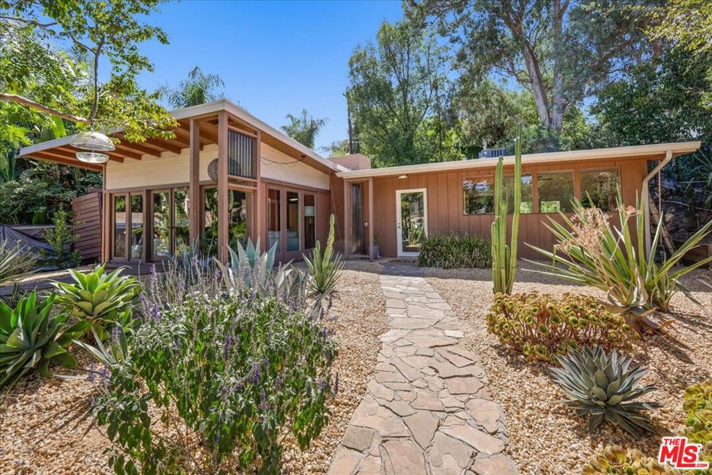 This stunning Mid-Century Modern architectural gem features a unique terraced setback and offers 4 bedrooms, 2.5 baths, and nearly 2,000 sq ft of thoughtfully designed living space. Designed with an ideal open floor plan, the home is divided into two distinct wings for privacy and functionality. The serene, spa-like primary suite features a luxurious soaking tub, a separate shower stall, and an adjoining room that is ideal for use as a nursery, office, or additional bedroom. The North Wing houses the remaining bedrooms, with both wings opening onto a central courtyard. The living areas have Mid-Century pebbled floors, while the bedrooms have all-new flooring. The kitchen has been updated with new appliances, while the entire home benefits from upgraded electrical systems, new lighting throughout, and fully paid solar panels for enhanced energy efficiency. The garage is a permitted ADU ideally situated adjacent to the pool, offering incredible versatility for guests, a studio, or a pool house. Surrounded by all-new landscaping, this tucked-away oasis seamlessly combines timeless historical details with clean, modern lines, making it a truly special place to call home.