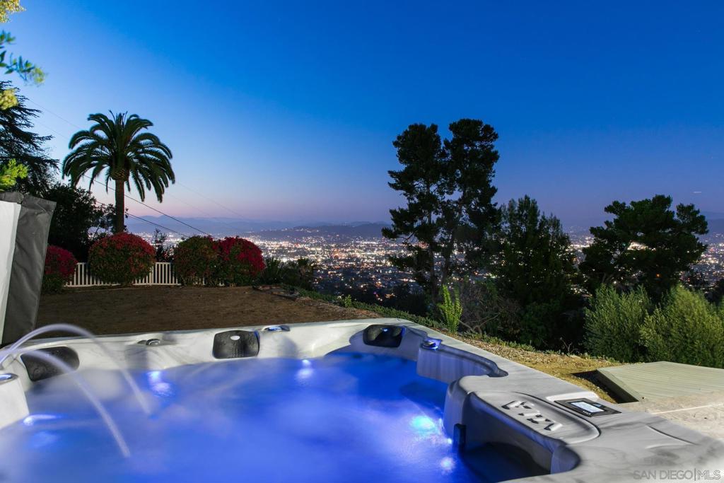 Nestled on a serene 0.63 acre cul-de-sac lot in coveted Mount Helix, this exquisite single-story residence offers sweeping panoramic mountain and city light views, refined upgrades, and a truly seamless indoor-outdoor lifestyle. A private courtyard with custom-stamped concrete welcomes you to striking double entry doors, opening into a voluminous living room where floor-to-ceiling glass doors fold away to frame the breathtaking natural surroundings. The open-concept layout flows effortlessly into the formal dining area and a designer-appointed chef’s kitchen featuring upscale custom wood cabinetry with soft close doors and drawers, quartz countertops, custom tile backsplash, high-end Thermador appliances, a generous walk-in pantry, and an oversized center island. The expansive family/living room with soaring ceilings connects to an impressive custom-built Trex deck—perfectly designed to preserve the natural beauty of the trees while embracing dramatic views and elevated entertaining. The tranquil primary suite is a true retreat, showcasing a custom walk-in closet and a luxurious spa-inspired ensuite with a jetted soaking tub, walk-in shower with built-in bench, bidet, designer vanity, quartz counters, and elegant lighting. Thoughtful enhancements include owned solar, a Trane HVAC system, new roof and gutters, Tesla charger, new garage door, fresh stucco, skylight, luxury vinyl plank flooring and recessed lighting throughout. The backyard oasis is equally functional and inviting, with a flat grassy lawn ideal for play and relaxation, an 8-person therapeutic spa with outdoor shower, and a wide driveway offering ample parking for RVs, recreational vehicles, and guests—plus rear backyard additional access. A separate laundry room features custom cabinetry and built-in organization, while the garage offers abundant storage. Ideally located just minutes from shopping, dining, top-rated schools, and freeway access, this is an exceptional opportunity to enjoy your own private piece of paradise in a truly remarkable and luxurious setting.