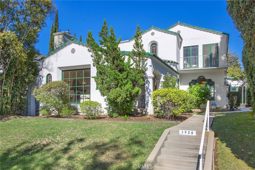 Nestled on one of Bixby Knolls’ most picturesque, tree-lined streets, this exceptional 1930s Spanish-style home is being offered for the first time in over 80 years. Lovingly maintained by the same family for generations, the home radiates warmth, history, and unmistakable pride of ownership. The main residence offers 2,795 sq ft, plus a 525 sq ft rumpus room with its own half bath, a three-car garage, and a versatile utility room (originally a garage) providing ample space, comfort, and ADU potential. The expansive front yard features mature landscaping and an authentic Spanish façade, setting the tone for the charm within. A gracious walkway leads to a serene, shaded side yard, ideal for relaxing, gardening, or entertaining. Inside, a dramatic entryway with vaulted ceilings, stained-glass windows, and a tiled stairwell welcomes you in. The formal living room is a showcase of elegance with original hardwood floors, Spanish sconces, a cozy decorative fireplace, French doors, and a large window flanked by stained glass. Off the living room, an office with built-in shelves offers flexibility as a guest space or fifth bedroom. The formal dining room connects seamlessly to a vintage-style kitchen with original cabinetry, hardware, and a beautifully restored 1930s Wedgewood stove. A charming breakfast nook with stained glass cabinetry completes the space. Downstairs also includes one bedroom and a full bath with original tile. Upstairs, the second bedroom features nearly floor-to-ceiling windows and French doors to a private balcony. The third bedroom offers a walk-in closet and alcove perfect for a desk or vanity. A second full bath retains its original tile with separate tub and shower. The fourth bedroom is an expansive suite with two rooms, multiple closets, and a private balcony—ideal for a primary suite with sitting area, nursery, or office. The rear of the property impresses with lush landscaping, utility basement, gazebo with new deck, and covered patio. Additional structures include the three-car garage, covered shed, and utility room. Above the garage, the inviting rumpus room, originally built in the 1940's, features a half bath and kitchenette. Brimming with character, this flexible space is ideal as a guest suite, studio, office, or potential income-producing ADU. 3928 Olive Avenue is a rare offering that blends historical charm with generous space and flexibility, all in one of Long Beach’s most desirable neighborhoods.