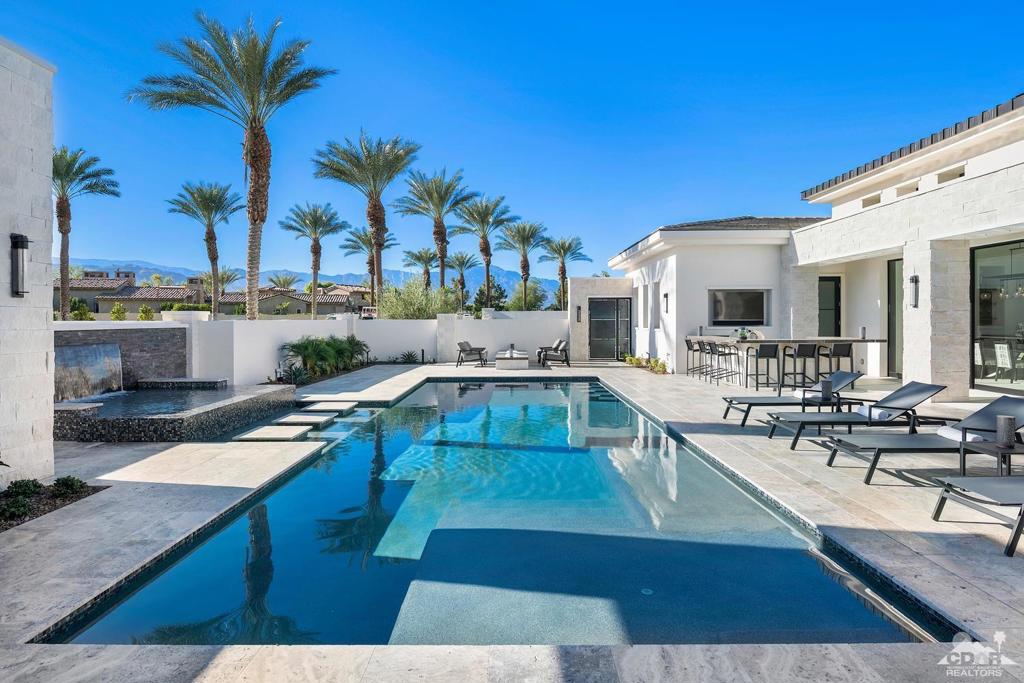 Located on one of the largest custom lots in desirable Toscana Country Club, this light-filled desert-modern home captures mountain and sunset views across the private south-facing front courtyard. Experience truly open indoor/outdoor living, dining and entertaining with five walls of disappearing glass opening seamlessly to a generous outdoor living room and patio surrounding the pool with cascading spa. Adjacent, the great room with grand fireplace and walk-behind wet bar, the state-of-the-art kitchen with huge island and butler's pantry will please the most discriminating chef and caterer alike. The luxurious master suite with fireplace includes two equally generous closets, large walk-in shower, dual vanities and water closets, and a private retreat to use as an office, sitting area or exercise room. The junior master suite with golf course view and a separate entrance guest house with its own living room, kitchenette and 2 en suite bedrooms, are sure to please family and friends.