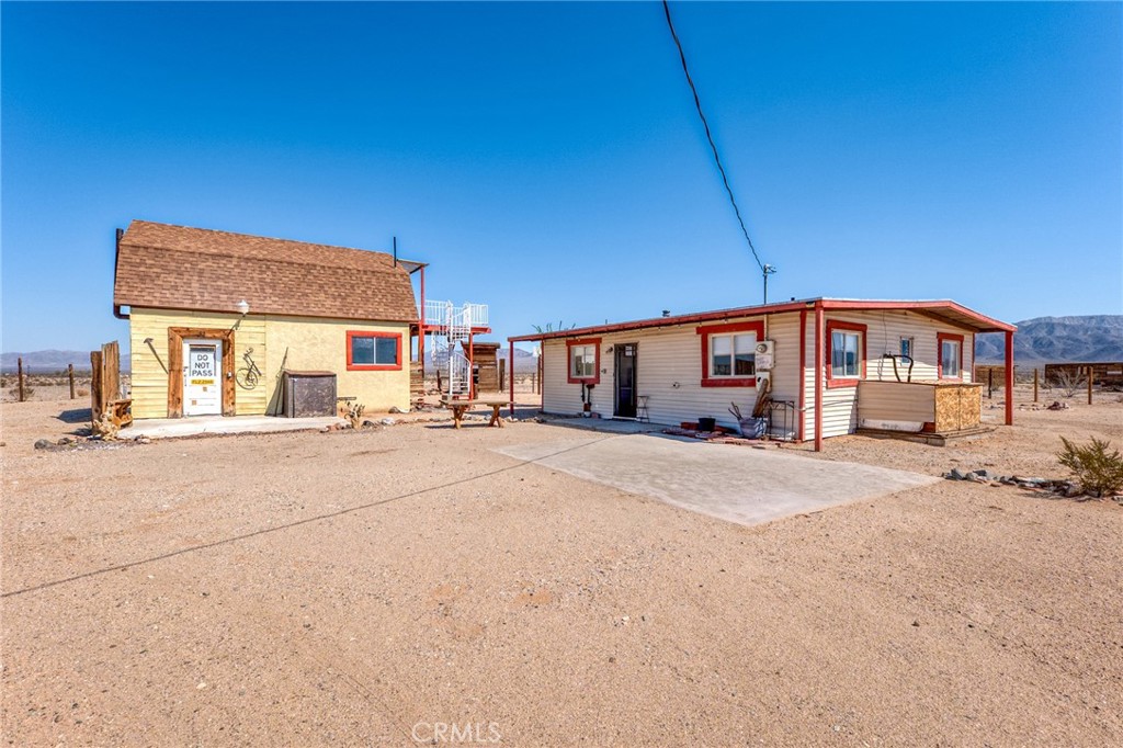 Set on 5 wide-open acres, this rustic 1958 2-bedroom, 1-bath home is brimming with potential. Investors, artists, and visionaries will appreciate the eclectic character and versatile layout. The main house features a light-filled open living area with sliding glass doors to the backyard, plus a cohesive kitchen/living space with bold red cabinetry that adds a fun vintage touch. The full bathroom includes a shower/tub combo and vessel sink. Natural light pours into every room, enhancing the home’s inviting atmosphere.
Beyond the home, a detached two-story barn expands the possibilities. Complete with plumbing, a half bath, and an upper-level deck with a spiral staircase, this space could be reimagined as a studio, workshop, guest quarters, or creative retreat. A fenced area around the house offers privacy and utility, while the expansive acreage leaves room to grow. The property is serviced by hauled water, providing flexibility for those seeking a low-maintenance option in the desert.
Enjoy star-filled skies at night, sweeping mountain views by day, and the creative energy that has made the High Desert a destination for artists, adventurers, and investors alike. Just minutes from The Palms Restaurant and a short drive into 29 Palms, this Wonder Valley property is ready to be transformed into a one-of-a-kind desert retreat.