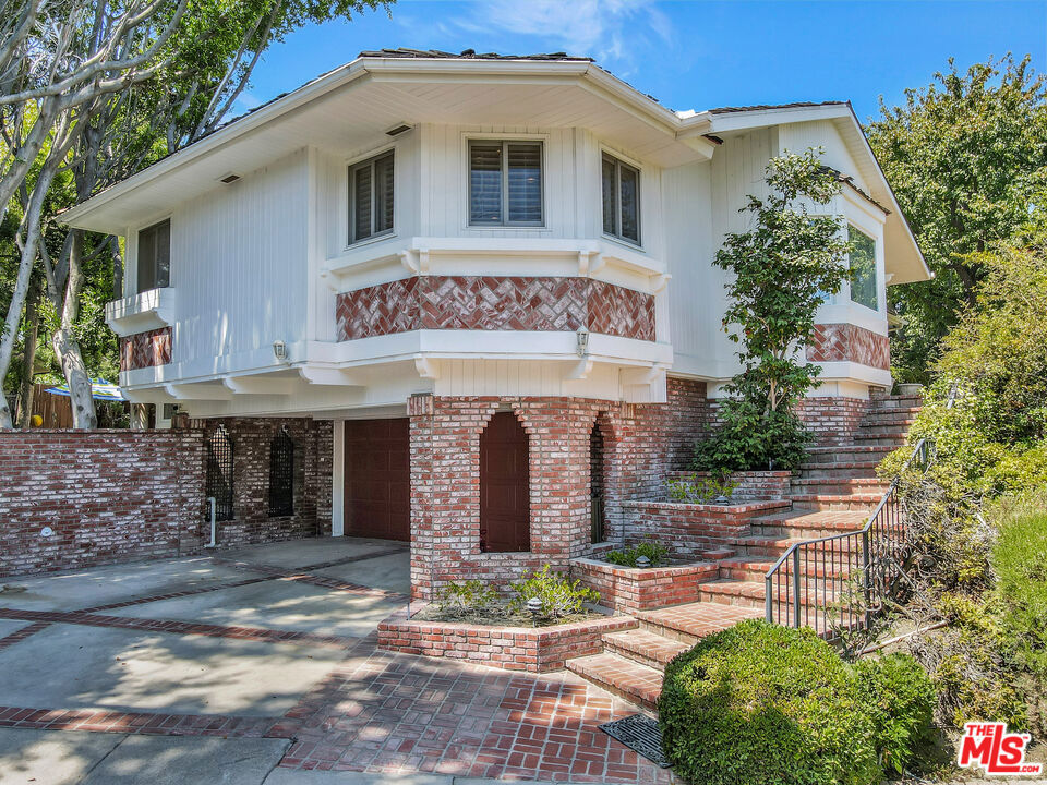 Set on a tree-dotted corner lot in Woodland Hills, this expansive 6-bedroom, 8-bathroom home impresses from the street with charming architectural details. The 5,334 SF home1,300 SF larger than the average residence in the area stands out from the rest. A grand entry with wooden double doors welcomes you inside the formal living room with high beamed ceilings and light glistening through bay windows. An ornate dining room is ready for you to host an elegant dinner party. The updated eat-in kitchen, outfitted with stainless steel appliances and an oversized island, offers the perfect spot for a breakfast nook surrounded by custom built-ins. Enjoy a well-appointed second living room, featuring a wet bar and French doors to the stunning backyard. The expansive home offers spaces for custom retreats and gatherings, such as the impressive library with custom-built-in floor-to-ceiling shelving, as well as a billiards room with ample windows and a beautiful beamed wood ceiling. Escape to the generous primary suite with a perfect sitting area and a spa-like bathroom with a soaking tub. The backyard is surrounded by large trees, which provide privacy for the resort-style pool with a waterfall feature. There are ample outdoor seating areas to enjoy the California breeze: you can sit by the pool, beneath the covered patio, or by the artfully designed koi pond for a taste of tranquility. This home is near highly-rated charter schools Serrania and Taft. There are plenty of shopping options close by on Ventura Blvd, including Whole Foods, Trader Joe's, and Target. Woodland Hills Country Club is under 2 miles away. Don't miss the opportunity to tour this exceptional Woodland Hills home!