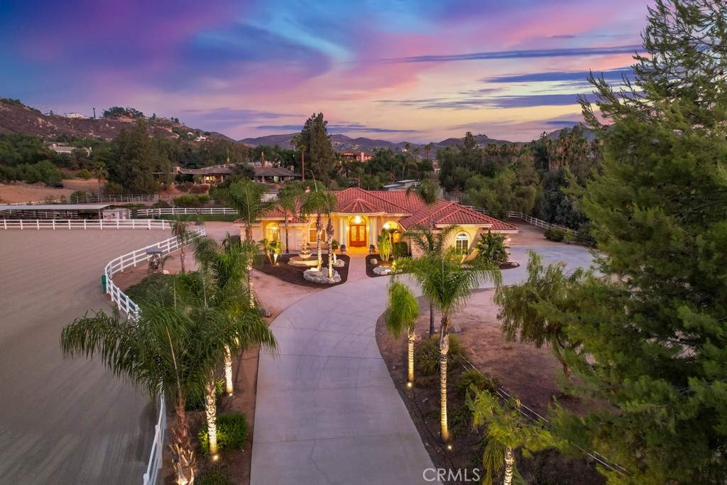 Luxurious Single-Story Executive Ranch with Horse Amenities on Over 2 Acres. Welcome to this extraordinary single-story executive ranch estate, a rare find combining luxury living with premier equestrian amenities, all set on over 2 fully fenced acres with automatic gate entrance. Designed for both elegance and function, the property offers immaculately manicured landscaping lined with palm trees, ensuring unmatched curb appeal and a private resort-like feel. Enter through the grand double door entry into soaring vaulted ceilings and a beautifully flowing open layout. Rich hardwood flooring graces the main living areas, while tile accents define the wet spaces. The expansive principal suite is a true retreat featuring a dual-sided fireplace, private lounge area, wet bar with beverage fridge space, and a spa-style bathroom with dual vanities, frameless glass double shower, jetted soaking tub, and linen closet. Additional highlights include a junior suite with private en suite, spacious Jack & Jill bedrooms, all with mirrored closets and ceiling fans. The gourmet kitchen is an entertainer’s dream, showcasing a massive island with wine rack and beverage fridge, pantry, stainless steel appliances, vegetable sink, trash compactor, and cozy breakfast nook that opens to a family room with fireplace. Enjoy year-round entertaining in the California Room with built-in outdoor cooking area. The fully equipped laundry room includes folding space, cabinetry, and granite countertops. For equestrian enthusiasts, this property is a dream come true with a fully fenced riding arena, three covered stalls, covered wash rack, automatic waterers, hot walker, and two sheds for tack and feed. Additional perks include RV parking and plenty of space for future enhancements. This is beautifully designed ranch estate that is a must see!