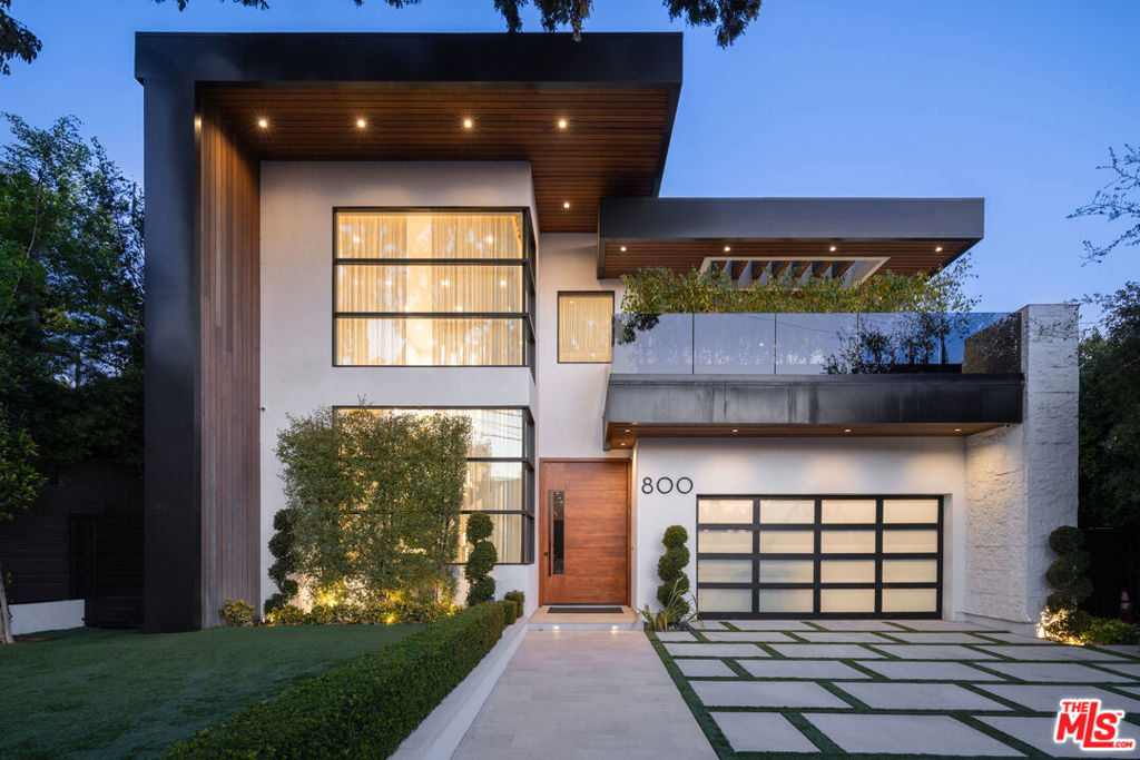 This modern architectural masterpiece in the heart of a prestigious hillside enclave boasts captivating panoramic views, from the cityscape to the Pacific Ocean. The entry foyer greets with a dramatic double-height ceiling and a grand walnut pivot door, while a sky-high stone fireplace feature wall defines the formal living room. The elegant dining room is highlighted by a bespoke marble-waterfall bar with easy access to the butler's pantry and family room. The chef's kitchen, with Miele and Wolf appliances, along with a Sub-Zero fridge, also offers a large central marble island extending into the breakfast dining area. The adjoining family room seamlessly connects to a spacious patio deck designed for alfresco dining and offering breathtaking vistas of the Getty Center. The main level also includes a refined stone powder room and a flexible office or guest suite. Upstairs, the luxurious primary suite is a retreat unto itself with dual walk-in closets, a stone fireplace, and a private balcony that frames sweeping views of downtown Los Angeles and the ocean. Its spa-inspired ensuite features a dual vanity, massive rain shower with steam, and a soaking tub. Additional ensuite guest rooms with balconies, a serene lounge area, and a well-appointed laundry room complete the upper level. The rooftop terrace offers the pinnacle of outdoor living, complete with a fire pit lounge, jacuzzi tub, and dining space, all surrounded by 360-degree, stunning vistas. The backyard showcases an infinity-edge pool, jacuzzi spa, and an outdoor kitchen with marble bar seating. A cold plunge, fire pit lounge, and flat lawn area add to the recreational appeal, while a fitness studio extends into a private weight-lifting zone. On the lower level, a classic suede-lined movie theater, expansive game room with foosball and pool table, as well as an infrared sauna (convertible to a wine cellar) offer ample entertainment. A spacious ensuite bedroom, additional powder room, and laundry facilities provide convenience. Floor to ceiling glass pocket doors open across all levels to the private backyard for seamless indoor-outdoor living. Designed with precision, the home features custom artful lighting, black steel accents, large-scale windows, and a sophisticated mix of Jerusalem stone and modern wood paneling on the exterior. A gated entry, two-car garage, ample storage, generator, and a basketball hoop complete the estate, offering tranquility and privacy on a quiet street minutes from world-class shopping and dining.