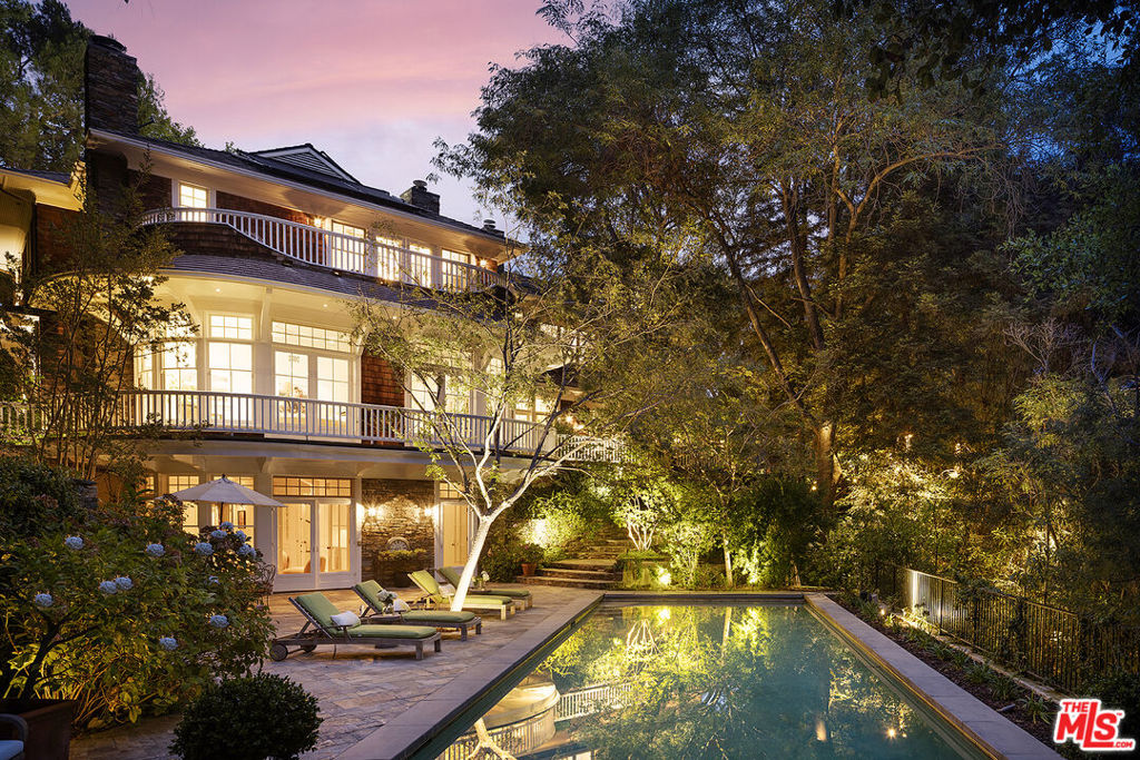 In beautiful lower Mandeville Canyon rests a magical gated private compound, hidden from the street and nestled up a long, tree-lined tranquil driveway. Situated on nearly one acre of lush grounds decorated by blossoming hydrangeas, cascading wisteria, and swaying trees, this rare find was designed by architect Lise Claiborne Matthews, AIA, ASID, and has never been on the market. Once the site of a historical botanical garden, the property spans two verdant parcels, fully encircled by beautiful mature trees for complete privacy. The enchanting facade opens to interiors that blend elegance and warmth, with soaring ceilings, curved glass windows, French doors at nearly every turn, and exquisite custom millwork throughout. Inside, the open-concept design encourages effortless entertaining. Guests are immediately met with a feeling of grand scale and sophistication, as they enter through the foyer and are met with the elegant dining room and formal living room with high architecturally custom-designed ceilings, functional curved glass windows, and anchored by a marble fireplace. Gorgeous greenery and filtered light is to be admired from every window of this stunning home. The living area features a cozy step-down family room with a media center and fireplace, while the chef's kitchen is equipped with a butcher-block island, three sinks, Viking range, Sub-Zero refrigeration, dual Miele dishwashers, and a pantry. A sunlit informal dining area and tranquil sunroom offer a serene setting for coffee, reading, or admiring the surrounding gardens. For grand occasions, the formal living room and dining room provide elegant settings for hosting gatherings, celebrations, and memorable evenings. The balance of the main floor contains an elegant guest suite, a large study, and a sixth bedroom. The expansive primary suite includes a sitting room, custom niches, French doors to a private balcony, and a spa-like bath with marble dual-sink vanity, oversized steam rainwater shower, soaking tub, dual water closets, dressing are, and two walk-in closets. Secondary bedrooms are spacious and full of charm, offering tranquil views of greenery and light throughout. On the recreational level, one would find an entertainment and wellness space with kitchenette, billiards room, sauna, cinema, gym, wine cellar, and a soundproof playroom, along with a light-filled atrium. Outside, the resort-style amenities include a sparkling 50-foot saltwater pool, meditation garden, koi pond, grassy lawn, patios, and lounging decks. Ample space allows for future additions such as a play area or sport court. Completing the estate is a three-car garage, a large fully functional gym or potential ADU, a large motor court, and additional parking accommodating twelve-plus vehicles. Offered furnished or unfurnished, this rare retreat is just minutes from Brentwood, Santa Monica, Pacific Palisades, and all the conveniences of the Westside, yet feels worlds away.