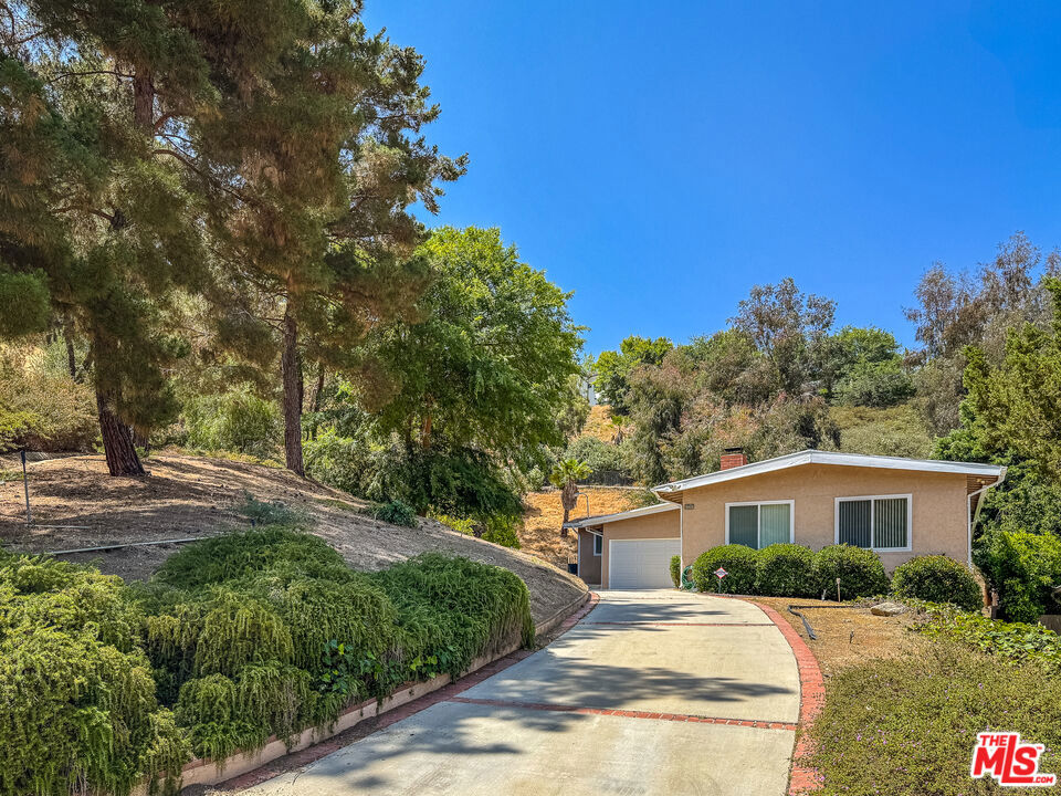 A rare opportunity south of the boulevard in Woodland Hills. Nestled above street level in a tranquil setting and surrounded by nature, this exceptional property offers the rare chance to restore or re-imagine a home in one of Woodland Hills' most desirable neighborhoods. Set on an expansive 8,775 sq ft lot with no neighbor on one side and adjacent open space, the property invites privacy and a serene, natural backdrop.The existing residence features 4 bedrooms and 2 bathrooms across approximately 1979 sq ft. Built in 1963, home features include a wood-burning fireplace (with gas line) anchoring the spacious living room, a large family room off the kitchen, patio area, double pane windows throughout for energy efficiency, built in speakers in several rooms, a newer 50 gallon water heater, newer KitchenAid double ovens, 6 ceiling fans, and newer garage door. The 2-car attached garage is distanced from the street and complemented by an additional one-car garage ideal for use as a studio, workshop, or bonus storage. There is ample space for additional parking. Laundry hookups are conveniently located in the garage. Whether seeking to renovate or build new, this is a special opportunity to create your dream home in a peaceful, established enclave just moments from shopping, dining, and top-rated schools.