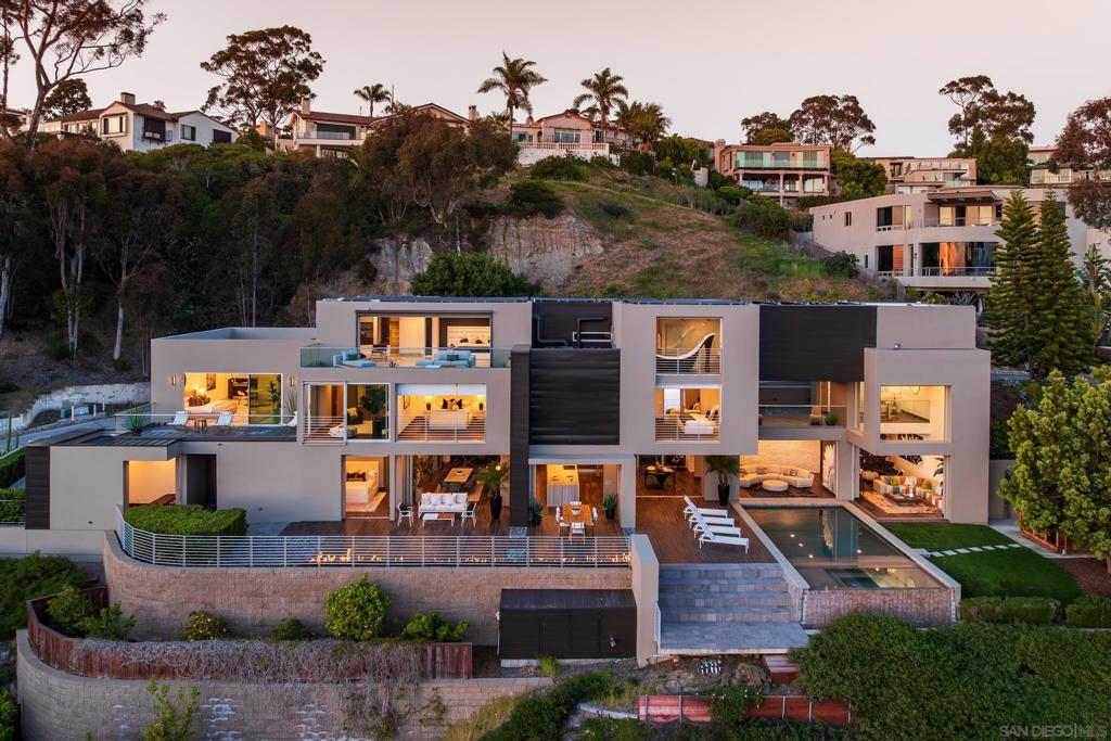 Perched above La Jolla’s prestigious Country Club, this award-winning contemporary estate by Jorge Ozorno is a true work of art. Designed to embrace the breathtaking surroundings, floor-to-ceiling glass walls fully retract to expansive decks and terraces, creating seamless indoor/outdoor living and capturing panoramic views of the Pacific Ocean, golf course, and village below. This minimalist masterpiece offers 6 bedrooms, 7 bathrooms, a private office, detached gym/yoga studio, infinity-edge pool and spa, sauna, and fire pit. The chef’s kitchen is outfitted with sleek custom cabinetry and a dramatic natural stone island—perfect for entertaining or quiet nights at home. The entire third floor is dedicated to the luxurious primary suite, featuring a private view deck, spa-inspired bath with a sculptural freestanding tub overlooking the ocean, and a newly reimagined boutique-style walk-in closet. Set on over half an acre with room to add a sport court, garden terraces, or outdoor lounge areas, this is a rare opportunity to own a timeless architectural statement in one of La Jolla’s most sought-after locations.