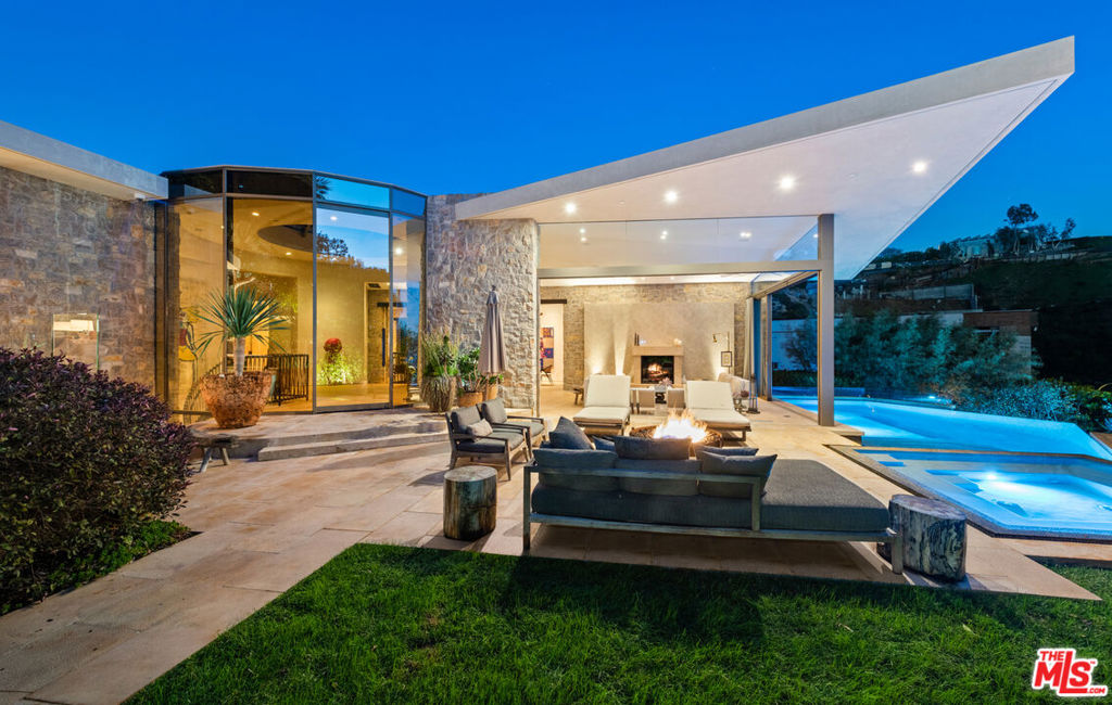 Embodying an organically modern aesthetic with its stone and glass facade, 9233 Swallow Drive takes up prominent residence in the highly coveted Bird Streets. Designed by the acclaimed Bradley Bayou, this five-bedroom, eight-bath masterpiece spans 7,308 square feet and offers tranquility above the bustling Sunset Strip. The open chef's kitchen, with Miele appliances and wood and stone accents, seamlessly integrates with a living/dining area bound by a dramatic two-sided gas fireplace. This space epitomizes the indoor/outdoor California lifestyle, with glass walls welcoming you into a harmonious exterior with panoramic city views. An ivy-covered facade and exquisite landscaping offer a verdant oasis, and among the fire pits, fireplace, multiple patios, and ample space for entertaining is the crown jewel: the infinity swimming pool with spa. More sanctuary awaits in the primary suite, with a fireplace, dual walk-in closets, and sliding glass doors that open to a private Zen garden and yoga deck. Indulge yourself with the ensuite bathroom's dual floating vanities, sunken tub, and marble steam shower, all accentuated by cool limestone flooring. The remaining four bedrooms are also ensuite, each with custom materials and elements for added distinction.Other amenities include a wet bar, library, gym, office, lounge, wine cellar, and four-car garage. A show-stopping feature is a luxe screening room with scarlet hues inspired by Radio City Music Hall. There's also a winding staircase and glass elevator for added touches of elegance, and smart-home technology to ensure 21st-century living at its finest. Nestled against the Hollywood Hills and on a corner lot, this home exists mere minutes from some of the best shopping, dining, and entertainment, but you'll love returning to this architectural treasure time and again.
