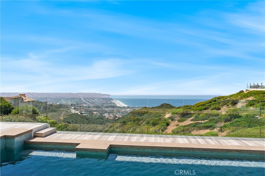 Set high above the coastline in the guard-gated enclave of Monarch Point, this newly transformed estate offers sweeping views from Dana Point’s cliffs to Monarch Bay’s coves. Every element of this hilltop retreat is curated for a refined lifestyle, blending indoor-outdoor living, modern style, and smart technology. A soaring 20-foot entry is crowned by a custom Murano glass chandelier. Floor-to-ceiling doors fill the home with light and open to a resort-style backyard with a pool, spa, porcelain deck, built-in DCS BBQ, and patio heaters—ideal for entertaining. The living room boasts a Napoleon linear fireplace framed in rare Black Carnelian stone, an 83” Sony Bravia TV, and five-speaker surround sound. A sleek bar with Sub-Zero fridges and Italian Cantoni cabinetry flows to a dining area with sunset views and a crystal chandelier. The chef’s kitchen features Thermador appliances, a Calacatta porcelain island, Fisher Paykel dishwashers, and a walk-in pantry. A breakfast nook sits beneath a glass chandelier and a frescoed ceiling by acclaimed artist Donovan Fitzgerald. The main level includes a private guest suite with separate entrance, kitchenette, full bath, and a Fitzgerald-painted ceiling. A dedicated office with LED lighting and custom shelving adds functionality. Upstairs, stainless double doors open to an ocean-facing primary suite with dual spa-like baths, walk-in closets, lounge with Napoleon fireplace and 83” Sony TV, and a full secondary kitchen. A Coverglass system opens to a wraparound balcony with panoramic views, fireplace, and another Fitzgerald fresco. Upgrades include new landscaping, pool/spa equipment with Aqualink, a 1,200-bottle wine cellar, tankless water heater, HVAC with Ecobee thermostats, Clare security with six Luma cameras, private elevator, Toto toilets, steam showers, and porcelain plank tiles throughout. Reverse osmosis systems serve all kitchens and bar sinks. A glass-floored landing under a skylight adds a striking architectural touch. Control4 automation and Lutron shades complete this smart coastal sanctuary. See Supplemental attachment for all the incredible details of upgrades!