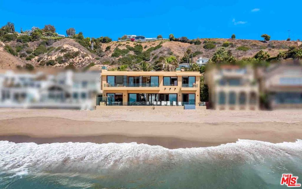 With 80 feet of beach frontage, non-stop sunrise-to-sunset ocean and island views, and magnificent, open interiors, this Carbon Beach contemporary is both private refuge and luxurious gathering place. Four separate decks and vanishing walls of glass define a lifestyle of relaxed elegance just steps from the sand. The ever-changing vistas take in a wave-fringed panorama from Point Dume to the Malibu Pier to the sparkling lights of the Queen's Necklace. A gated entry opens into a spacious, palm-lined courtyard leading to the glass front door, which offers a first tantalizing view of the ocean. Within, tranquil, ocean-view spaces are luminous with Portuguese limestone floors, wide windows, and the serene illumination of an enormous atrium skylight. With gorgeous built-in wood cabinetry and gallery walls suitable for a museum-quality art collection, the indoor-outdoor living room opens seamlessly to a full-width beachfront deck complete with ceramic tile floors, al fresco dining area, ample seating, Lynx barbecue center, and built-in tiled hot tub. Inside, the spectacular entertaining space features a fireplace, a wet bar, a conversation lounge, and a beautiful dining area that opens into an interior garden courtyard. The adjacent kitchen is equipped for the professional chef, with generous wood cabinets, granite countertops, an island with bar seating, soffit lighting, a chandelier breakfast area, and sliding doors to the oceanfront deck. Also on the home's main level are two en-suite bedrooms, one currently serving as a gym, plus a powder room. On the upper floor, accessible by stairs or elevator and arrayed around a mezzanine-style walkway beneath the atrium skylight, there are three oceanfront suites, each with a view balcony, and a laundry room with a dog-washing station. The primary suite is a serene retreat with fireplace, large walk-in closet, spa-style bath, and a separate office with sink and beverage cooler. The home has numerous smart-home features, including three-zone air conditioning, security, central vacuum, water filtration, and more. There is garage parking for three vehicles, with a second washer dryer in the garage, plus additional guest parking in the front courtyard. Located on one of Southern California's most desirable stretches of coastline, this stunning architectural residence is both contemporary and timeless.