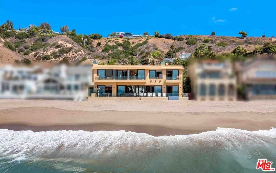 With 80 feet of beach frontage, non-stop sunrise-to-sunset ocean and island views, and magnificent, open interiors, this Carbon Beach contemporary is both private refuge and luxurious gathering place. Four separate decks and vanishing walls of glass define a lifestyle of relaxed elegance just steps from the sand. The ever-changing vistas take in a wave-fringed panorama from Point Dume to the Malibu Pier to the sparkling lights of the Queen's Necklace. A gated entry opens into a spacious, palm-lined courtyard leading to the glass front door, which offers a first tantalizing view of the ocean. Within, tranquil, ocean-view spaces are luminous with Portuguese limestone floors, wide windows, and the serene illumination of an enormous atrium skylight. With gorgeous built-in wood cabinetry and gallery walls suitable for a museum-quality art collection, the indoor-outdoor living room opens seamlessly to a full-width beachfront deck complete with ceramic tile floors, al fresco dining area, ample seating, Lynx barbecue center, and built-in tiled hot tub. Inside, the spectacular entertaining space features a fireplace, a wet bar, a conversation lounge, and a beautiful dining area that opens into an interior garden courtyard. The adjacent kitchen is equipped for the professional chef, with generous wood cabinets, granite countertops, an island with bar seating, soffit lighting, a chandelier breakfast area, and sliding doors to the oceanfront deck. Also on the home's main level are two en-suite bedrooms, one currently serving as a gym, plus a powder room. On the upper floor, accessible by stairs or elevator and arrayed around a mezzanine-style walkway beneath the atrium skylight, there are three oceanfront suites, each with a view balcony, and a laundry room with a dog-washing station. The primary suite is a serene retreat with fireplace, large walk-in closet, spa-style bath, and a separate office with sink and beverage cooler. The home has numerous smart-home features, including three-zone air conditioning, security, central vacuum, water filtration, and more. There is garage parking for three vehicles, with a second washer dryer in the garage, plus additional guest parking in the front courtyard. Located on one of Southern California's most desirable stretches of coastline, this stunning architectural residence is both contemporary and timeless.
