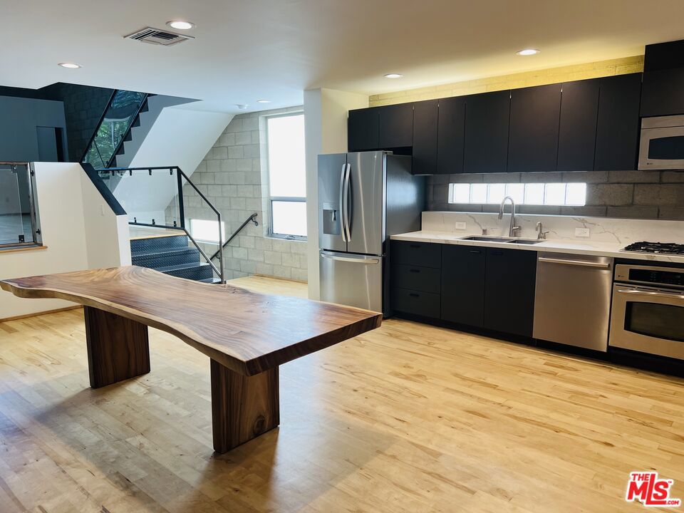 Tri-level Live/Work Townhome Loft is perfectly located in the Melrose Design District. A corner unit and only 4 total units in the complex. Ideal as a personal residence with business, creative-space, an art gallery, production or design studio, entertainment, multimedia, start-up company or as a cool loft-style home. Created of steel, cement block, and glass, the modern tri-level loft features an entry level that hosts a large open concept area with a half bath and direct access to a 4-car private garage (or utilize the garage for an expansive work space for a total of approx 3000sqft of living space). The second level consists of a kitchen with quartz counters and stainless appliances, flexible private rooms and open-concept spaces with soaring double-height ceilings, a full bath, and adjacent atrium. A third level creates a primary suite or additional creative space with a full bath with dual vanity and access to an additional 350sqft outdoor sun deck, outdoor meeting area or alfresco dining space for entertaining with views of the Hollywood Hills. Laundry located in the garage, with hardwood and concrete floors, and recessed lighting throughout. Centrally located to Hollywood, and adjacent to infamous eateries: Osteria & Pizza Mozza, art and design galleries, and studio shops. Also listed for sale $1,995,000.