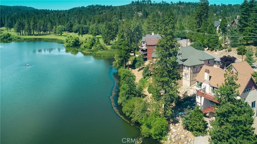 Discover luxury mountain living in this stunning 5-bedroom lakefront retreat, uniquely positioned on the shores of Grass Valley Lake and adjacent to the Lake Arrowhead Country Club golf course. One of only five exclusive properties with true water frontage, this custom-built home showcases captivating views of the lake, fairways, and surrounding ridgelines. Perfect for golf enthusiasts, the home includes direct golf cart access to the course, plus expansive views of the greens right from your own backyard. Inside, you'll find an inviting blend of comfort and elegance — from the spacious living room with a dramatic stone fireplace and floor-to-ceiling picture windows that perfectly frame the lake, to the chef’s kitchen featuring a massive island, KitchenAid appliances, custom alder cabinetry, and a wine fridge. The adjacent dining room with its own cozy fireplace is perfect for memorable gatherings. Downstairs offers a flexible living space with a family room that opens to a lake-view deck, complete with spa tub. The private primary suite includes serene lake views, dual-sided fireplace, a spa tub, and a steam shower. Two guest bedrooms and an additional full bath complete the lower level. Step outside to a newly updated outdoor entertaining area with a gas fire pit, bar, and lounge seating in a lush, secluded setting. Bonus features include a separate guest suite/ADU, Generac generator, dual-zone central heating and A/C, fresh exterior paint, and low-maintenance stucco siding. The two-car garage is complemented by a dedicated golf cart garage with direct access to the course. An additional lot with RV parking is available for purchase. Enjoy coveted Lake Rights to private Lake Arrowhead—ideal for boating, waterskiing, and fishing. A rare and remarkable offering for those who love the water, the mountains—and the game.