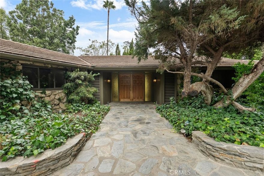 Welcome to 1218 Flintridge Avenue, a breathtaking sanctuary nestled in the picturesque city of La Canada Flintridge! This stunning mid-century modern single-family pool home exudes elegance and comfort, featuring 3 generously sized bedrooms and 3 beautifully designed bathrooms that seamlessly blend contemporary flair with inviting warmth. Set on an expansive 56,866 sq. ft. lot, this property is adorned with lush greenery, creating the perfect retreat for relaxation. A long, private driveway leads to a gated entry, providing ample parking and ensuring ultimate privacy. The meticulously landscaped grounds offer panoramic views of the majestic mountains, enhancing the serene atmosphere. Inside, the residence showcases enchanting beamed coffered ceilings and ambient lighting that create a bright and airy environment, complemented by charming ceiling fans that provide a refreshing breeze. The expansive living room beckons relaxation, complete with a cozy brick-walled fireplace inviting you to unwind. Plush carpeting graces the living room, dining room, and bedrooms, while sturdy hardwood flooring flows throughout the remainder of the home. The kitchen is a true culinary masterpiece, boasting a breakfast counter, built-in electric stovetop, double ovens, stylish range hood, dishwasher, and generous cabinet space—transforming it into an entertainer's delight. The inviting dining area is perfect for enjoying meals and is conveniently located near a tastefully designed half bathroom. The bright and airy bedrooms offer ample space for personalization, with the primary suite featuring a luxurious en-suite bathroom that includes a chic double sink vanity, spacious walk-in shower, separate bathtub, and bidet. The additional bathrooms showcase relaxing shower-in-tub combinations and another walk-in shower, while a dedicated laundry area with built-in storage enhances functionality throughout the home. Outside, your private backyard oasis awaits, complete with a sparkling pool and spa overlooking the city, providing breathtaking views, along with a private BBQ area and ample greenery, perfect for savoring beautiful weather and unwinding in tranquility. Located in a prime area, this home offers an unparalleled sense of privacy surrounded by lush landscaping while still being a short drive away from an array of restaurants and shopping centers, ensuring both convenience and tranquility.